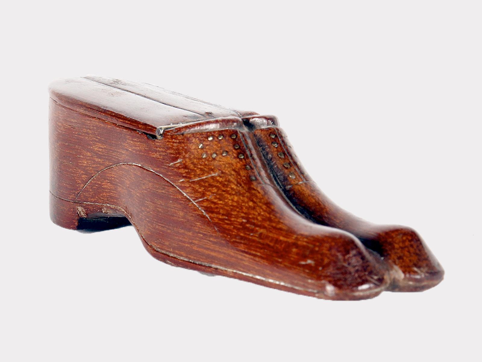 La tabacchiera è realizzata in legno di nocciola intagliato e raffigura un paio di scarpe. La parte superiore si apre, con un coperchio che rivela il contenitore del tabacco. I tacchi, le suole e i lacci sono evidenziati da una decorazione piqué.