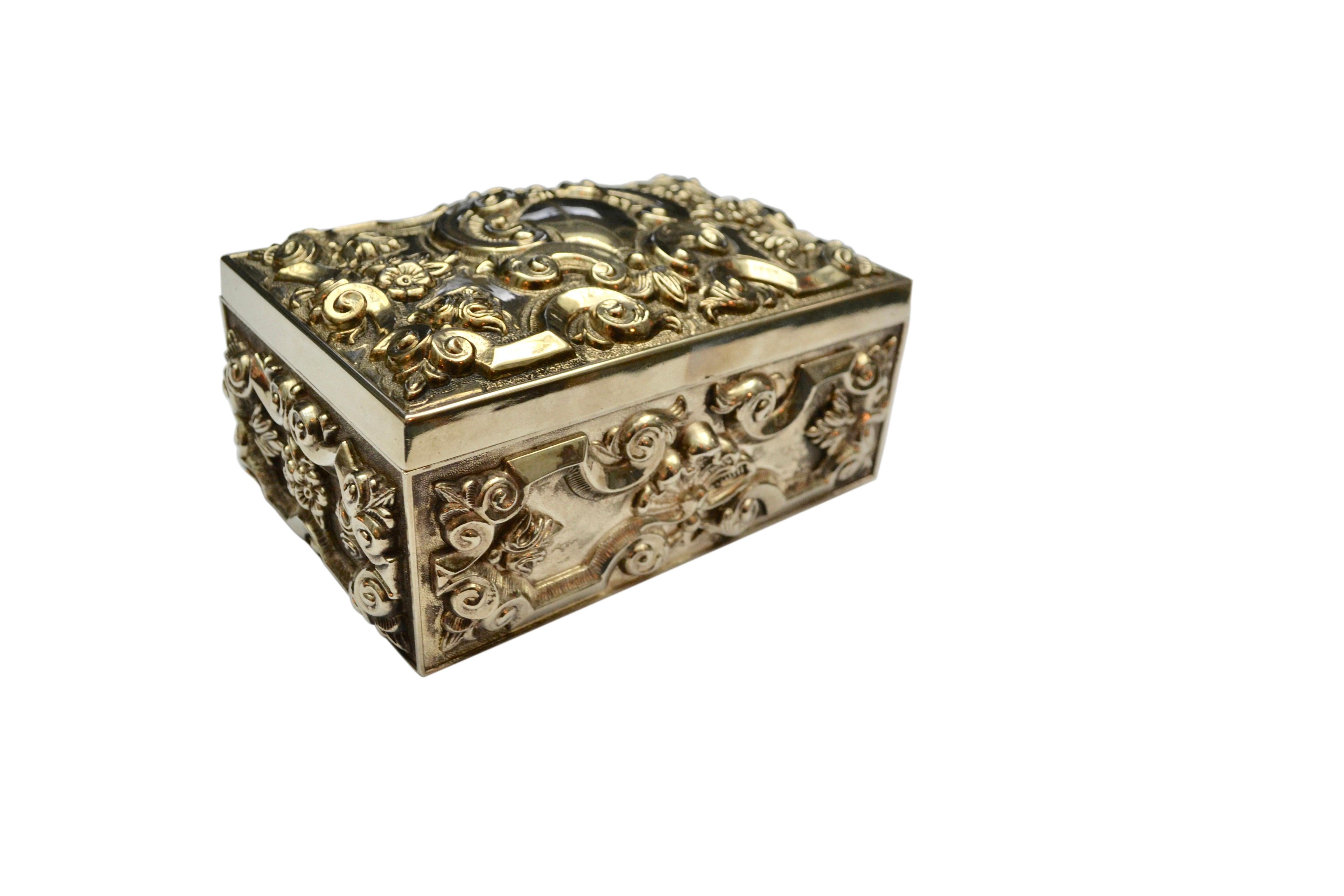 A heavy silver-plated jewellery box with overall scroll work raised on the top and four sides. The overall design includes flowers, scrolls, etc. and the top features a shaped medallion which was likely meant for an engraved name or monogram. The