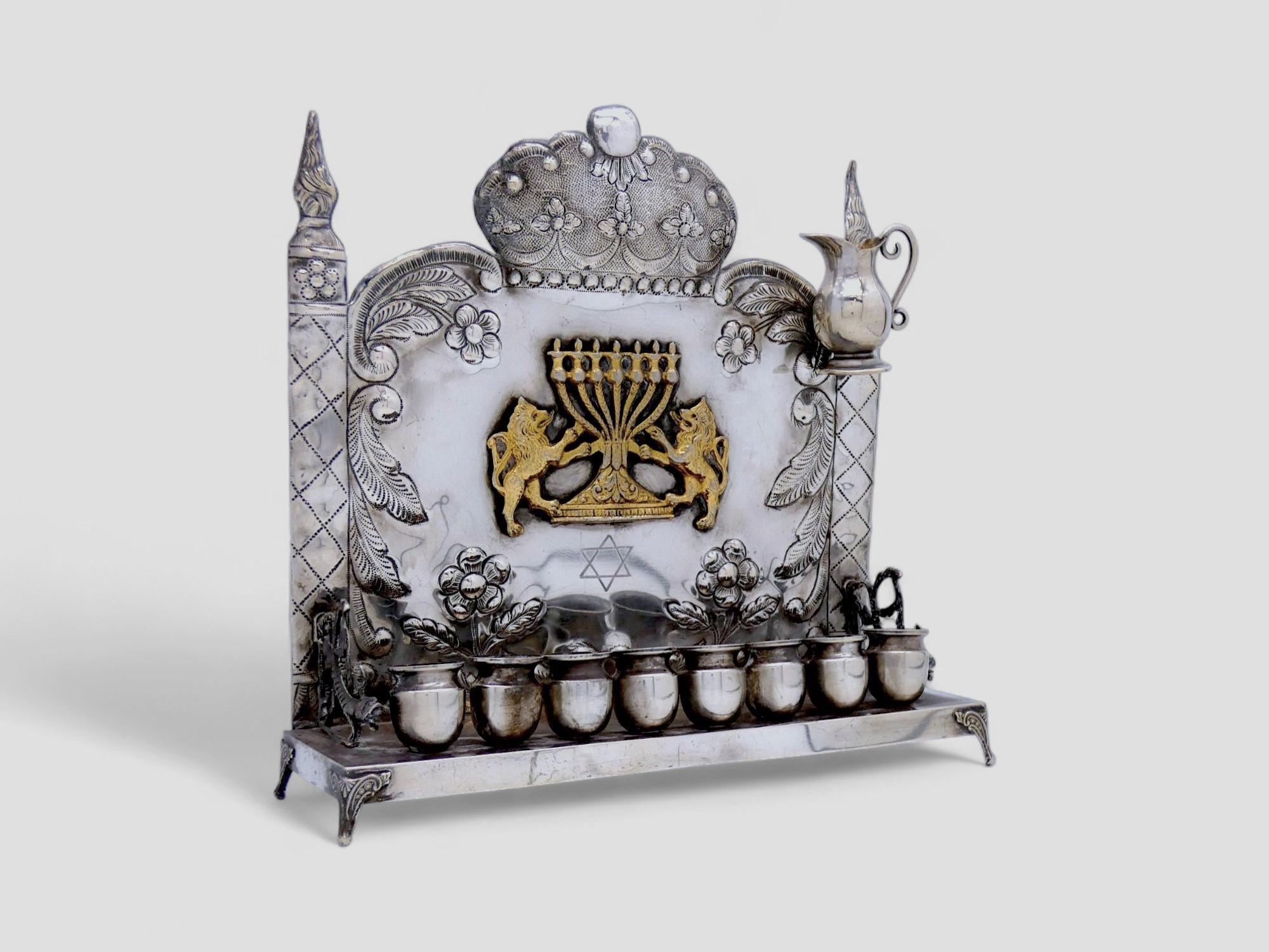 Impresionante lámpara de Hannukah americana, repujada a mano y con diferentes animales y diseños florales con distintas representaciones.

La placa posterior está bellamente bordeada con flores cinceladas y motivos foliados drapeados enmarcados por