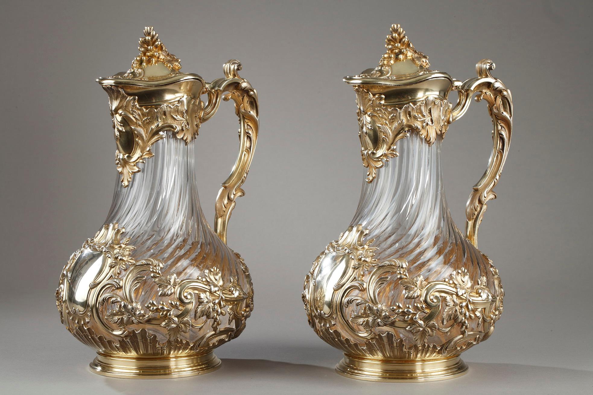 Important pair of carafes or jugs in orangeade in blown crystal, cut and twisted. The crystal is set in a silver and vermeil setting. The collar includes a cartouche decor, asymmetrical rocky patterns. The grip in high relief is adorned with a
