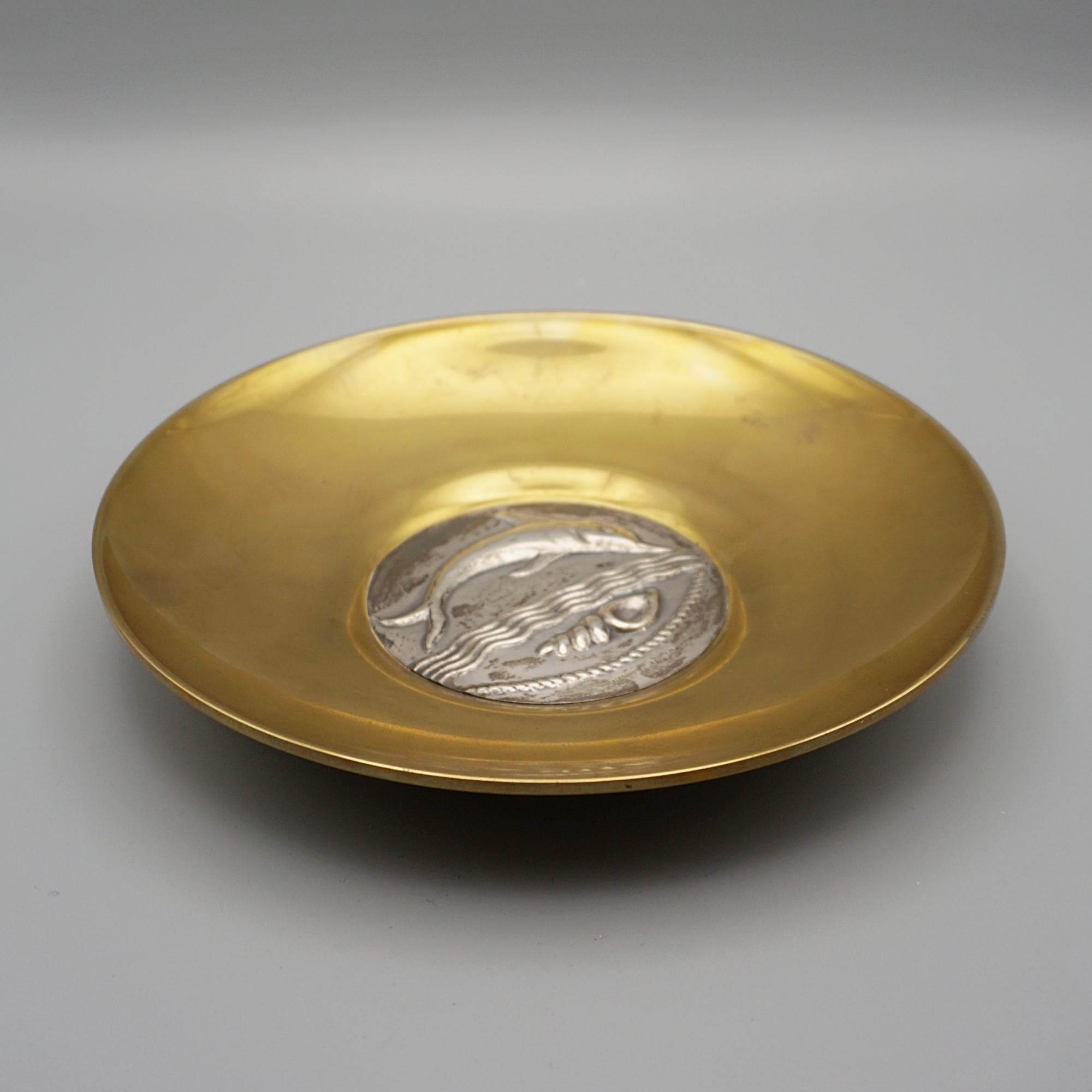 Un plat en argent massif et en vermeil conçu par Ilianis Lalaounis (1920-2013). La pièce centrale représente un dauphin sautant au-dessus d'un coquillage. Estampillé 900 Lalaounis au recto.

Dimensions : H 3,5 cm, P 20 cm : H 3.5cm, D 20cm

Origine