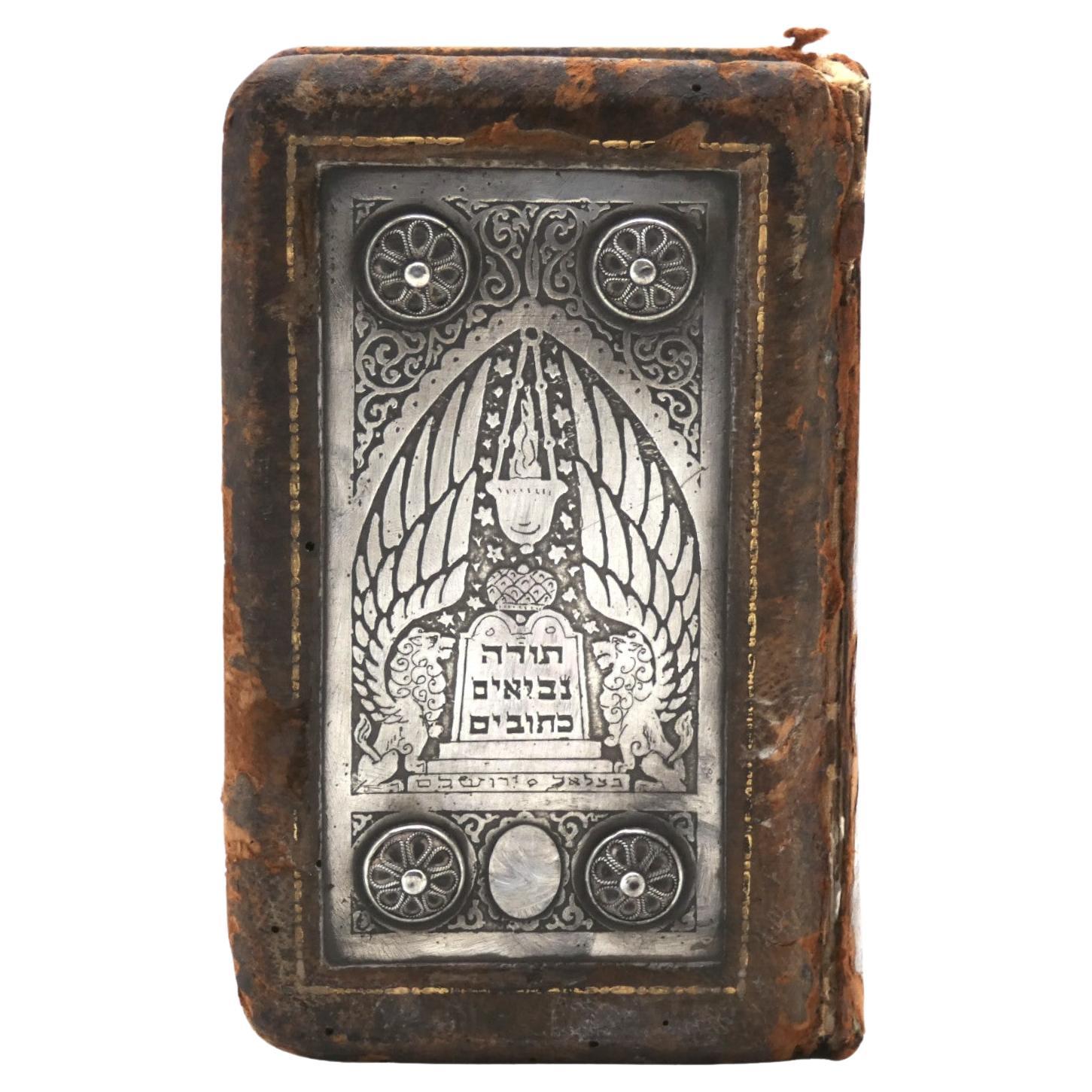 Una rilegatura in argento e pelle di Bezalel di Israel del 1940 circa è un pezzo importante di Judaica. Bezalel, il nome associato alla Bezalel School of Arts and Crafts di Gerusalemme, è noto per il suo significativo contributo all'arte e