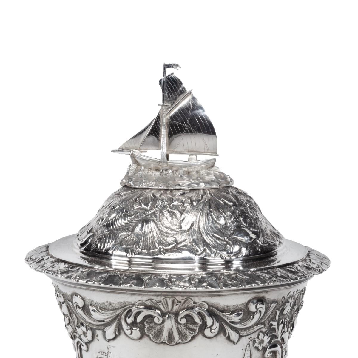 A silver and silver-gilt sailing regatta trophy by Samuel Hayne and Dudley Cater, 1838, embossed on each side with gaff cutters racing above a presentation inscription and surrounded by scrolling acanthus, shells, scrolls and flowers, with shell