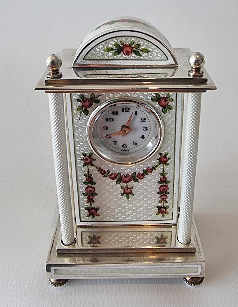 A fine and very unusual shaped silver and white guilloche enamel carriage or boudoir clock. The engine turned white guilloche enamel with overpainted swags of flowers and roses. The case with two front pillars also in white guilloche enamel,