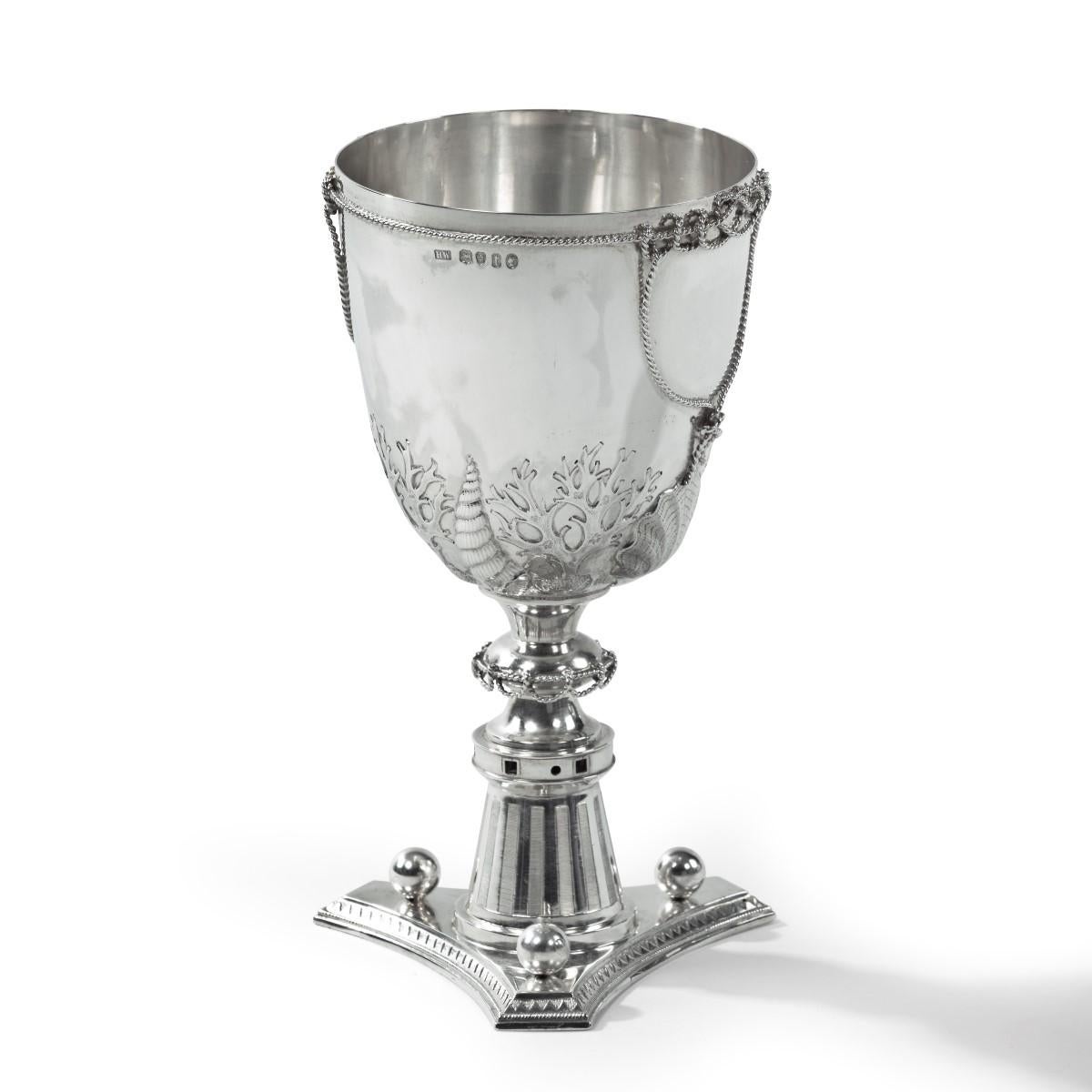 A silver cup by Henry Wilkinson, dated 1874, the goblet embossed and chased with seaweed fronds and seashells, applied with twisted and looped ropes around the rim, foot and blank central cartouche, all raised upon a tripod capstan base with three