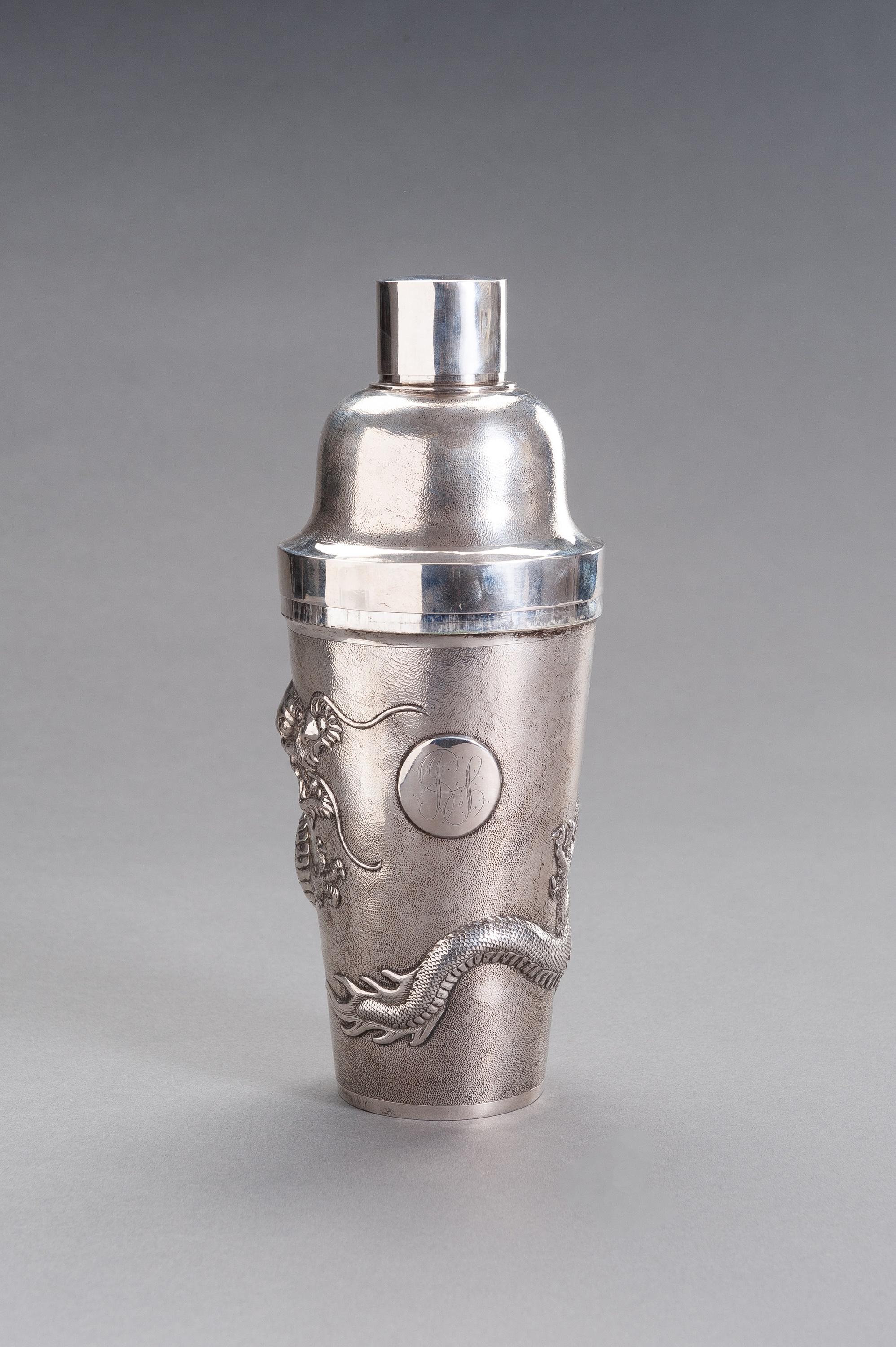 Ein silberner Drachen-Cocktailshaker, China, um 1920

Er besteht aus drei Teilen, dem Schüttelkörper, dem Filterbecher und dem Deckel. Die ersten beiden tragen einen Hammerschlaggrund, der Korpus ist zusätzlich mit einem geprägten und gravierten