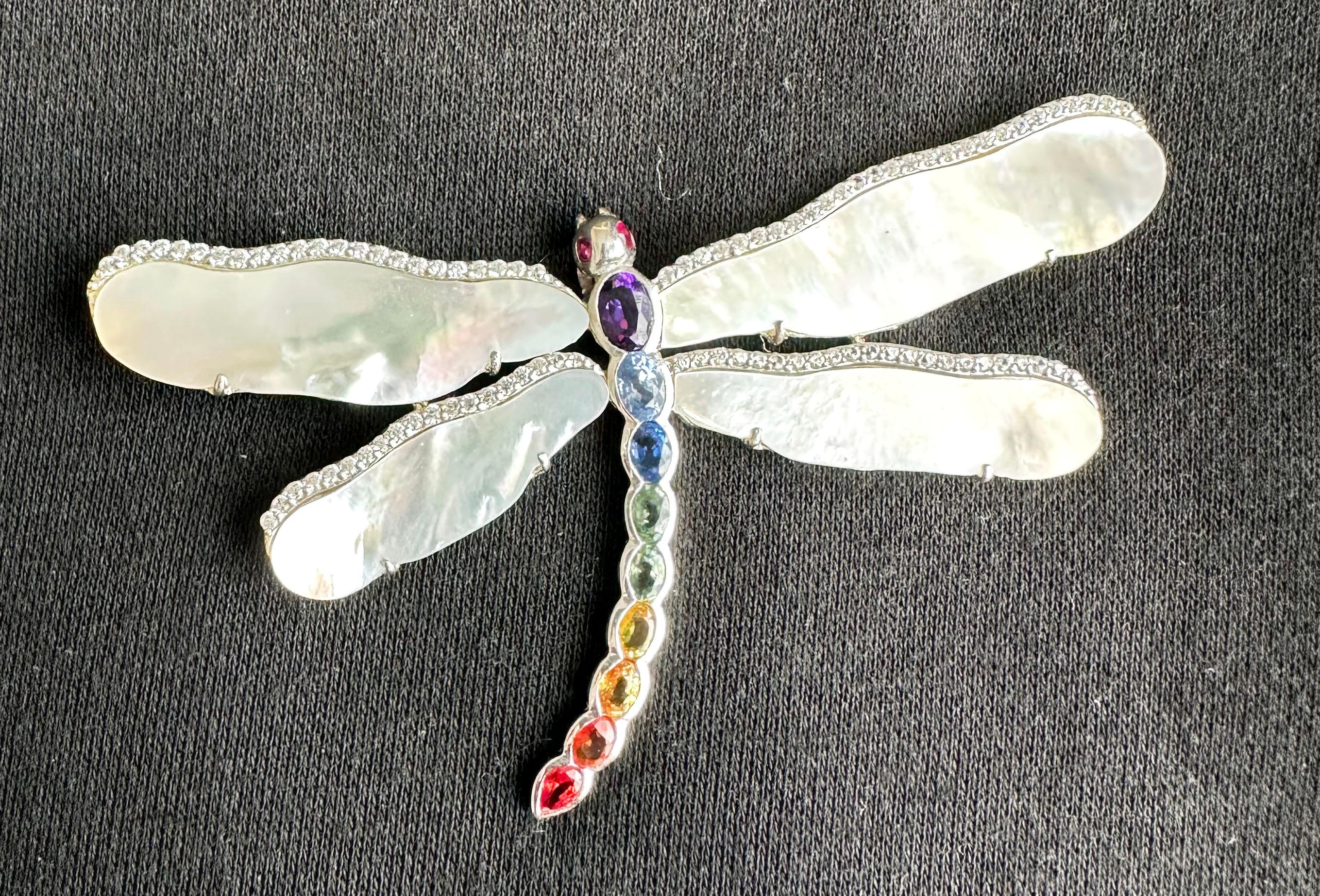 This one of a kind piece is convertible between a Brooch and a Pendant. It is set with Mother of Pearl Wings accented by tiny White Sapphires. The Body is set with a Rainbow Collection of Sapphires and an Amethyst and Ruby Eyes. The head has a bail