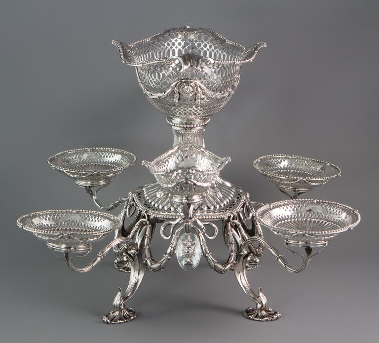 The epergne with seven detachable baskets or dishes, the arms and baskets or dishes each numbered & marked, the central basket with engraved oval heraldic shield to either side, the baskets & dishes each with an engraved seated unicorn crest. The
