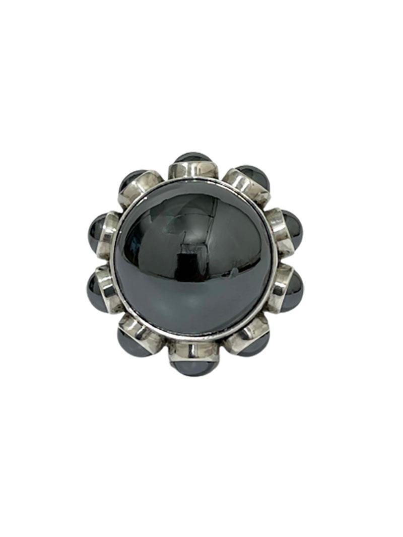 A silver Georg Jensen Design ring by Astrid Fog, Denmark 1971

A Hematite cabochon mounted ring designed by Astrid Fog, surrounded with 10 Hematite cabochon mounted small stones
Hematite is a strong grounding, purifying and protective stone.