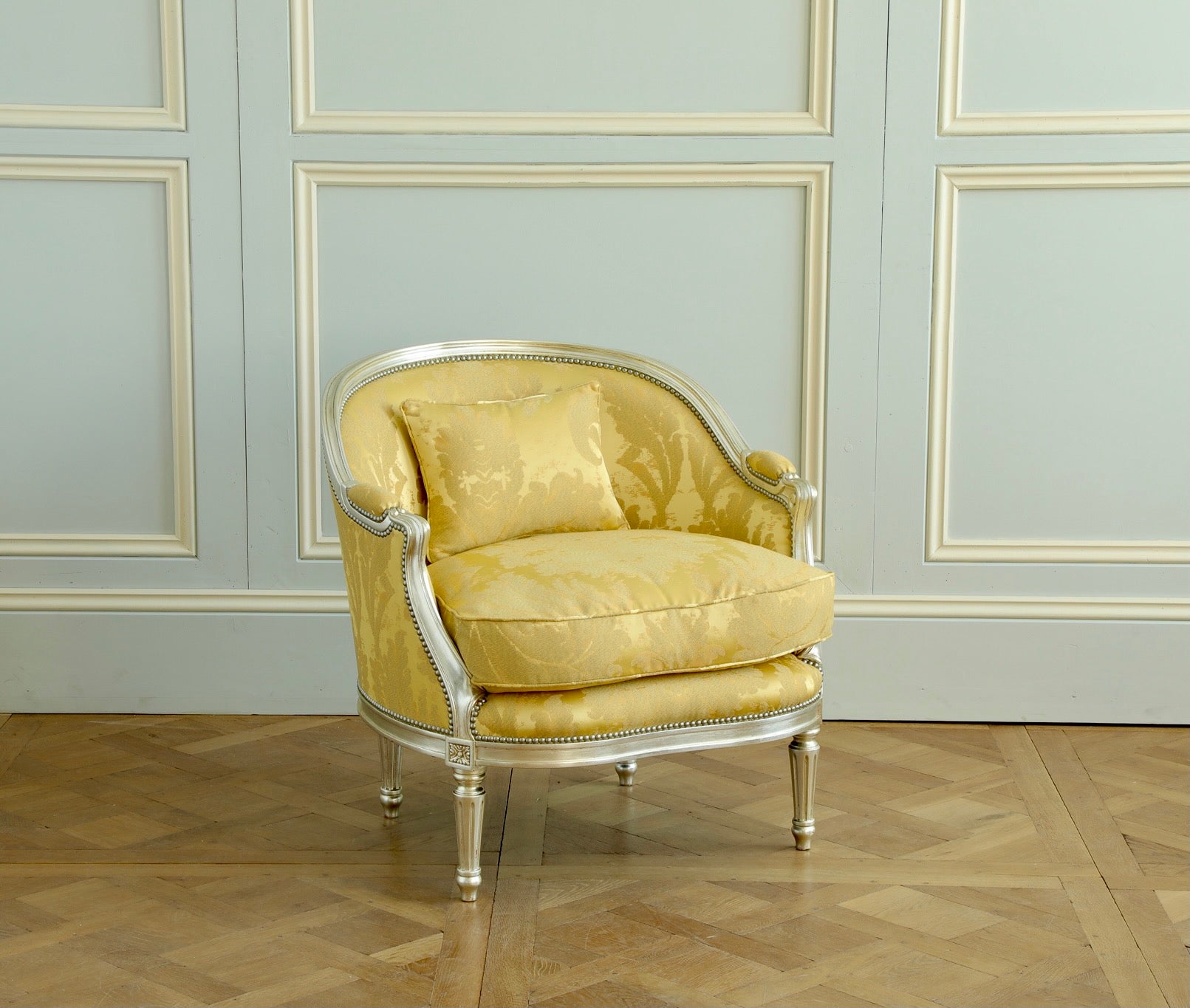 A  Hollywood Regency style marquise armchair featuring elegant curves and a glamorous silver gilt wood finish. The chairs have a plump feather seat cushion for comfort and are upholstered in an Italian fabric by Rubelli with a blue scatter cushion