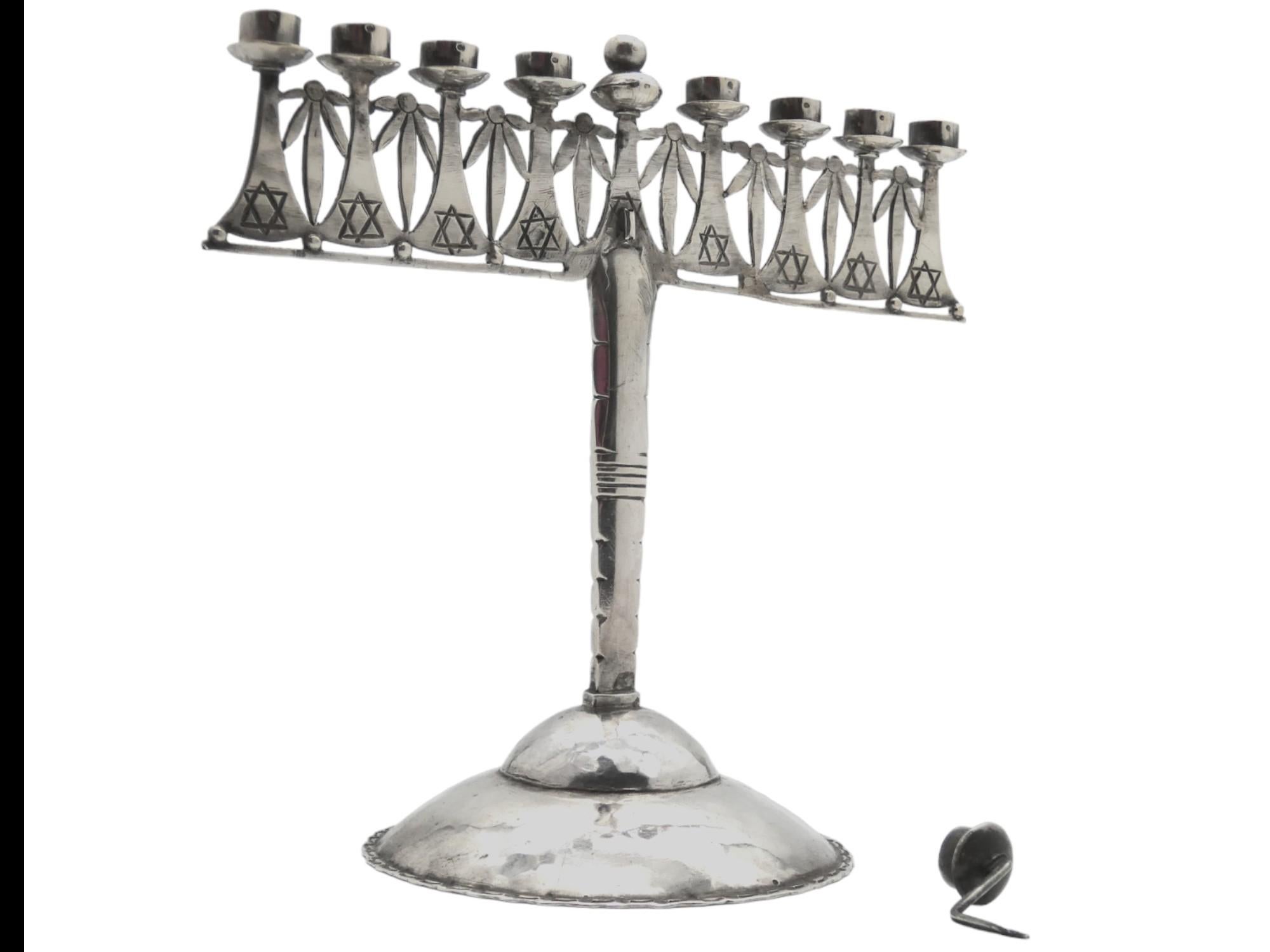 Lámpara de Hanukkah artesanal de plata única, fabricada en Alemania hacia 1930.

Esta Lámpara de Hanukkah es realmente única y tiene unos cuantos estilos diferentes de artesanía y diseños que componen su estructura. Parece que esta menorá está hecha