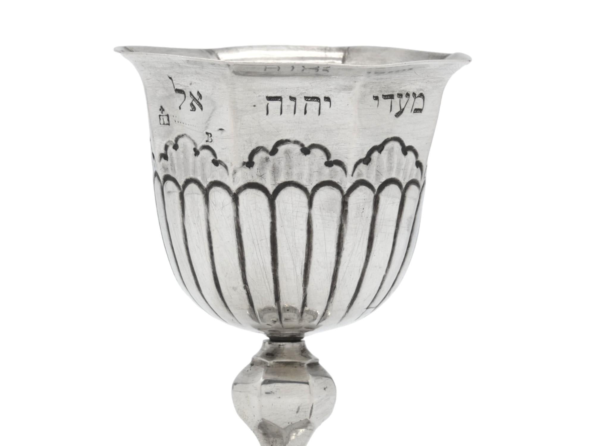 Ein bedeutender Kiddusch-Kelch aus Silber, hergestellt in Deutschland im 18. Jahrhundert.

Der Kelch steht auf einem runden, gewölbten Sockel, der von einem floralen Rankenwerk umrahmt wird.

Ein geknickter Trophäenstiel stützt den Hauptkörper, der