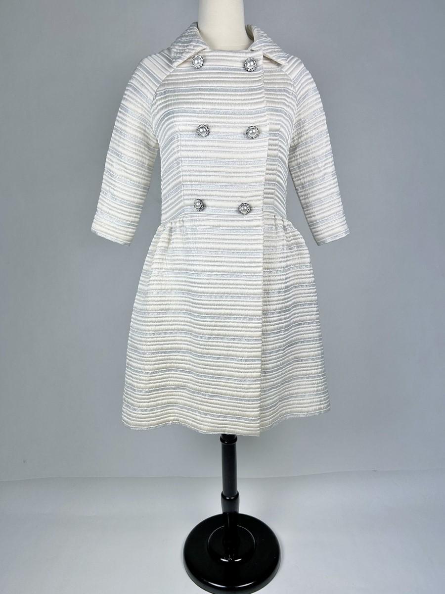 Circa 1960-1963
France
An unidentified haute couture jewel-buttoned formal coat dating from the early 1960s. Double-breasted at the front with folded panels, long raglan sleeves, skirted effect by side pleats. Back in white silk satin with silver