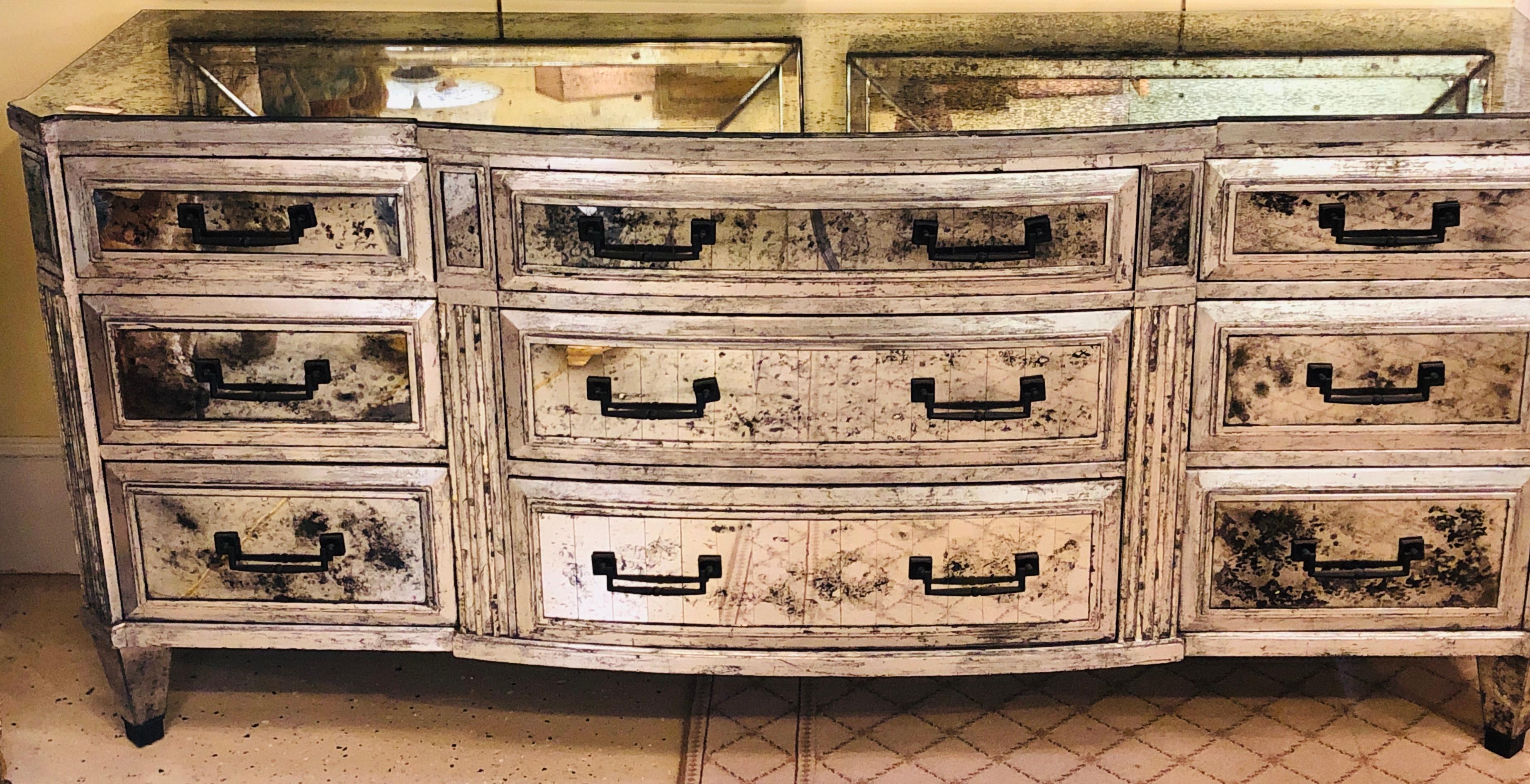 A stunning silver leafed and antiqued mirror designer Hollywood Regency bow front dresser sideboard. The antiqued mirror recessed into the fine silver leafed wood frame on this custom quality sideboard or triple dresser having nine drawers. The