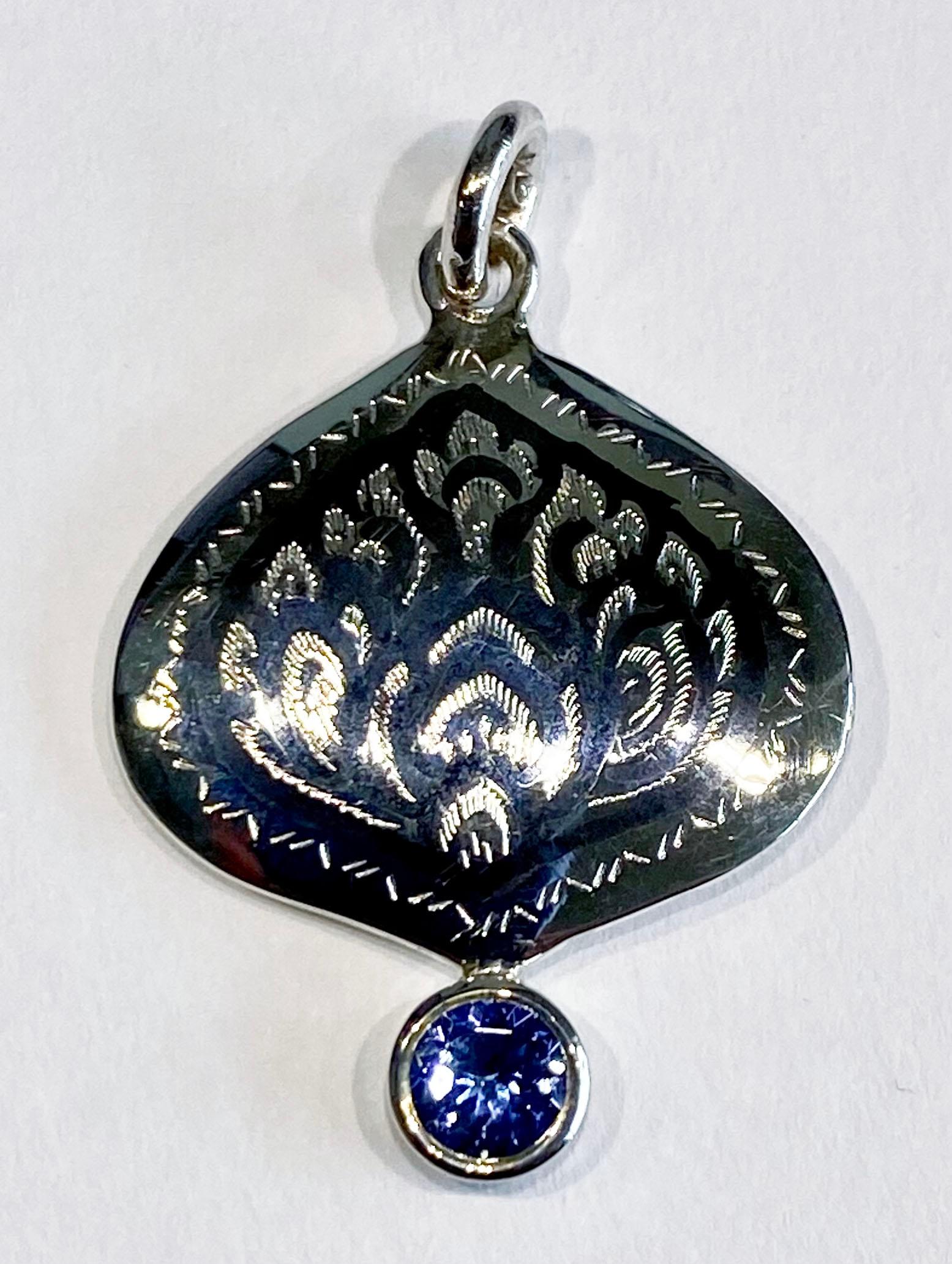 A Silver Filagree Pendant Accented with Tanzanite. The style of Silver work is called Nielloware and is a silver craft that comes from Southern Thailand. This is a one of a kind pendant accented with a 5MM Round Blue Tanzanite. The pendant hangs
