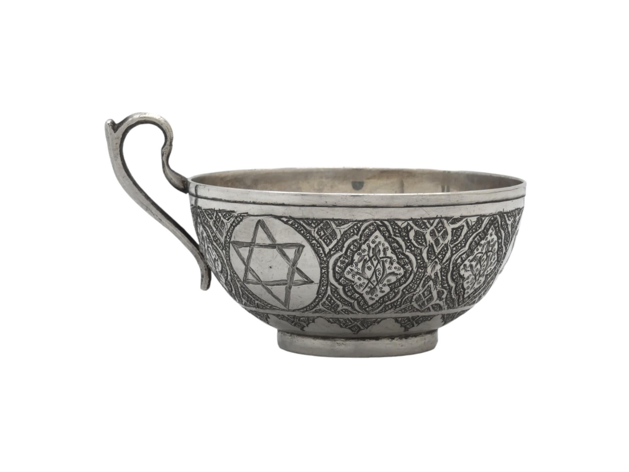 A silver Persian Kiddush cup and complementing tray from Iran circa 1920, crafted in a teacup form, is a beautiful example of the region's rich cultural and artistic heritage. This piece of Persian silverware used for Shabbat displays the exquisite