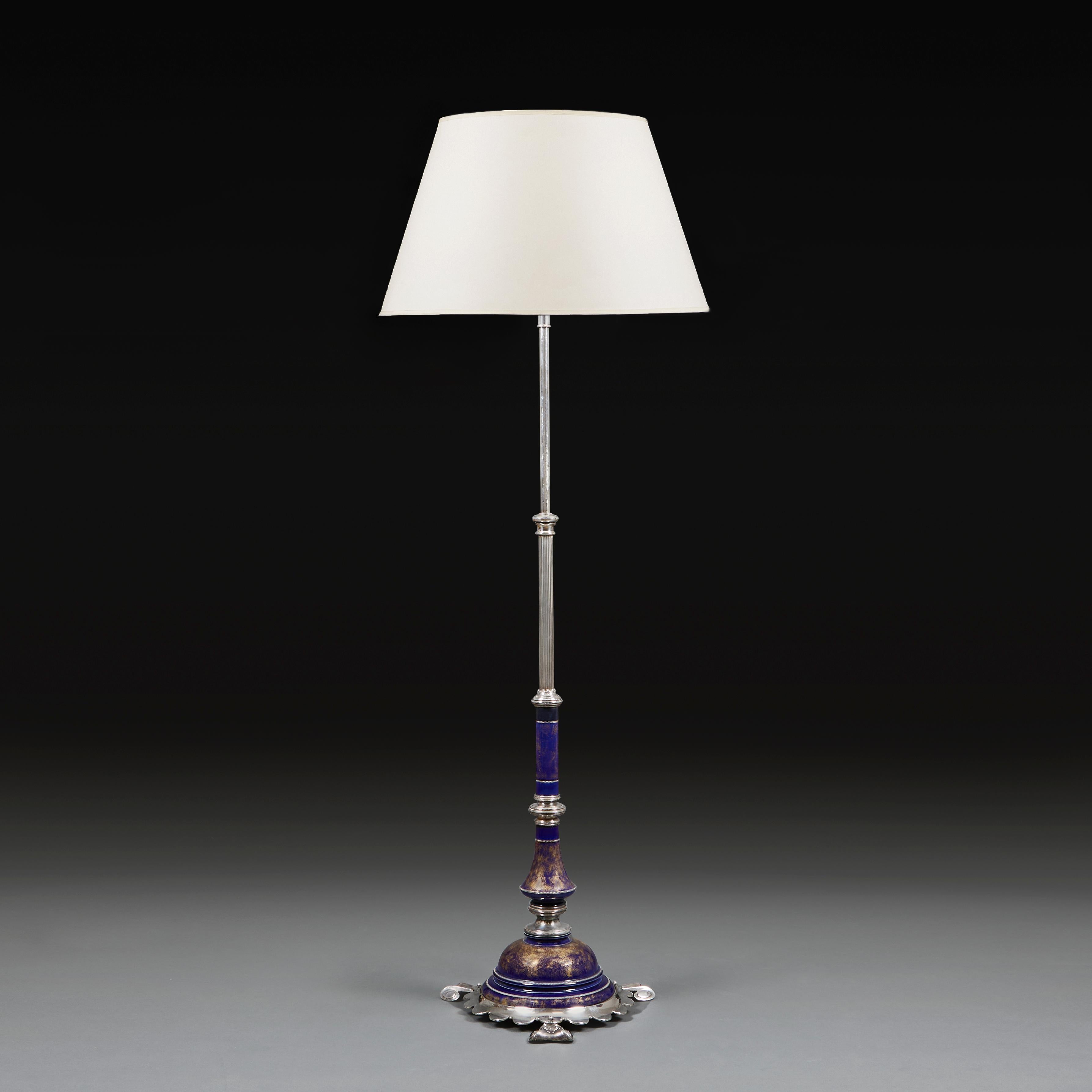 An unusual Edwardian standard lamp in silver plate, with contrasting blue and gold enamel sections to the base, with adjustable stem, and all supported on a scalloped base with three scroll feet.
England, circa 1910. 
Height of column   