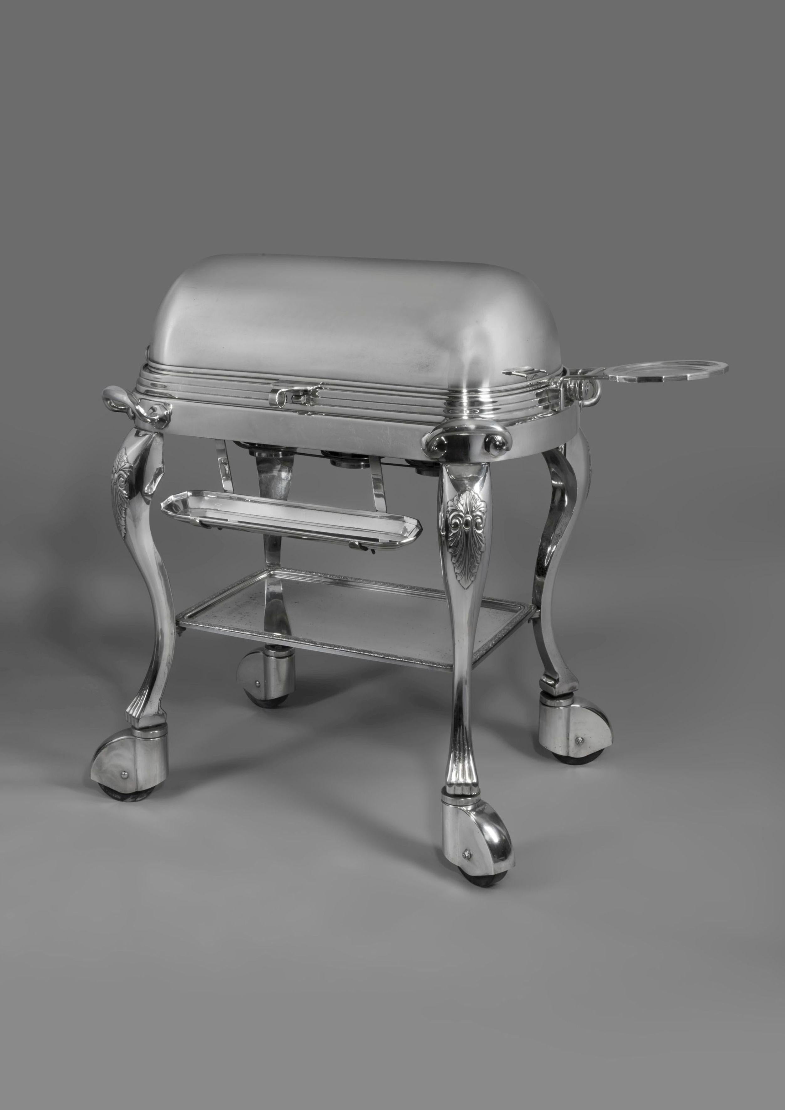 A silver plated roast beef trolley.

American, circa 1910.

The roll top lid opening to reveal a warming tray fitted with a removable carving board and two reservoirs, over three burners, with a coaster to one side and an oblong utensil rest to