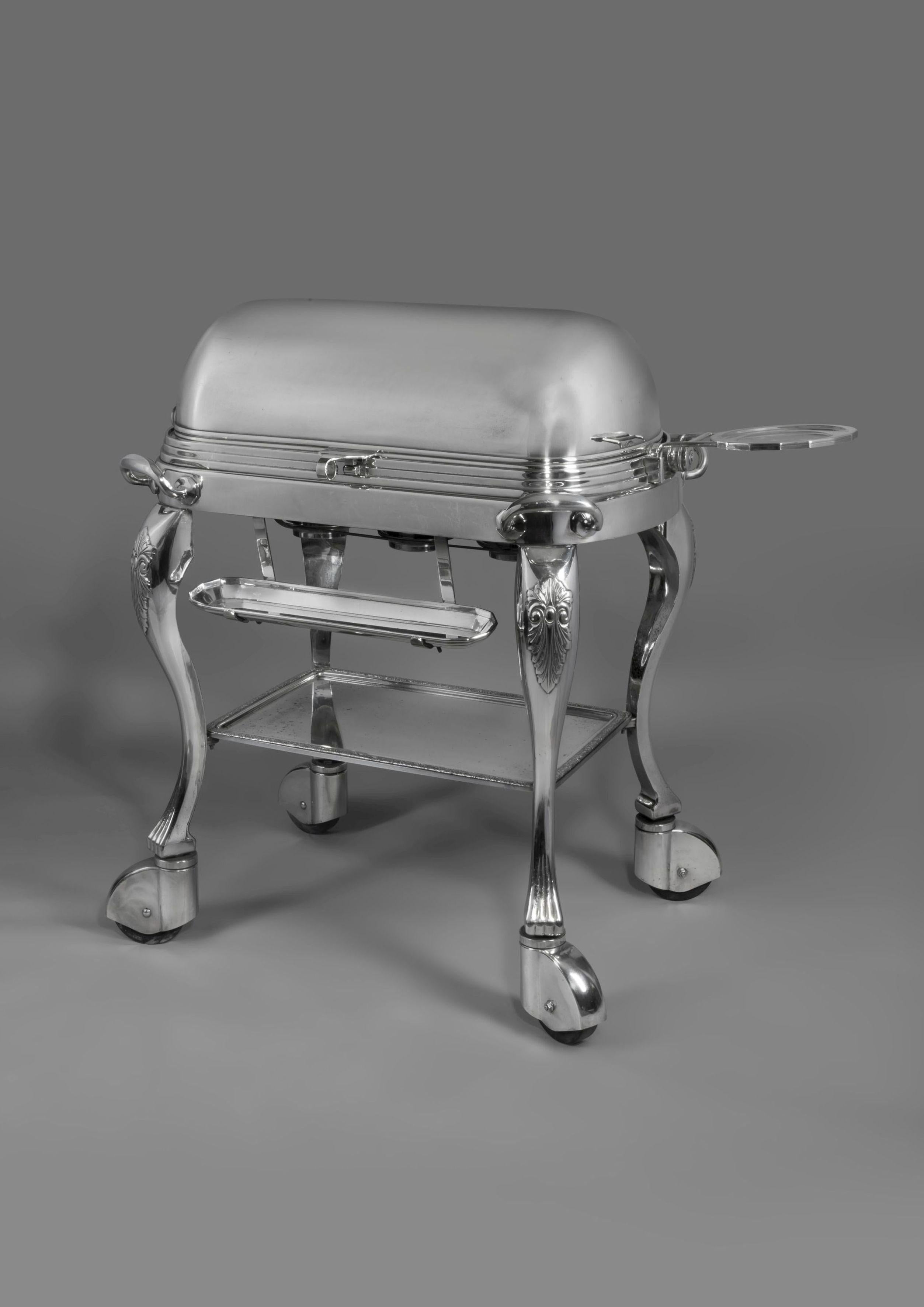 Un carrito de carne asada bañado en plata.

Estadounidense, hacia 1910.

La tapa superior enrollable se abre para revelar una bandeja calientaplatos equipada con una tabla de trinchar extraíble y dos depósitos, sobre tres quemadores, con un