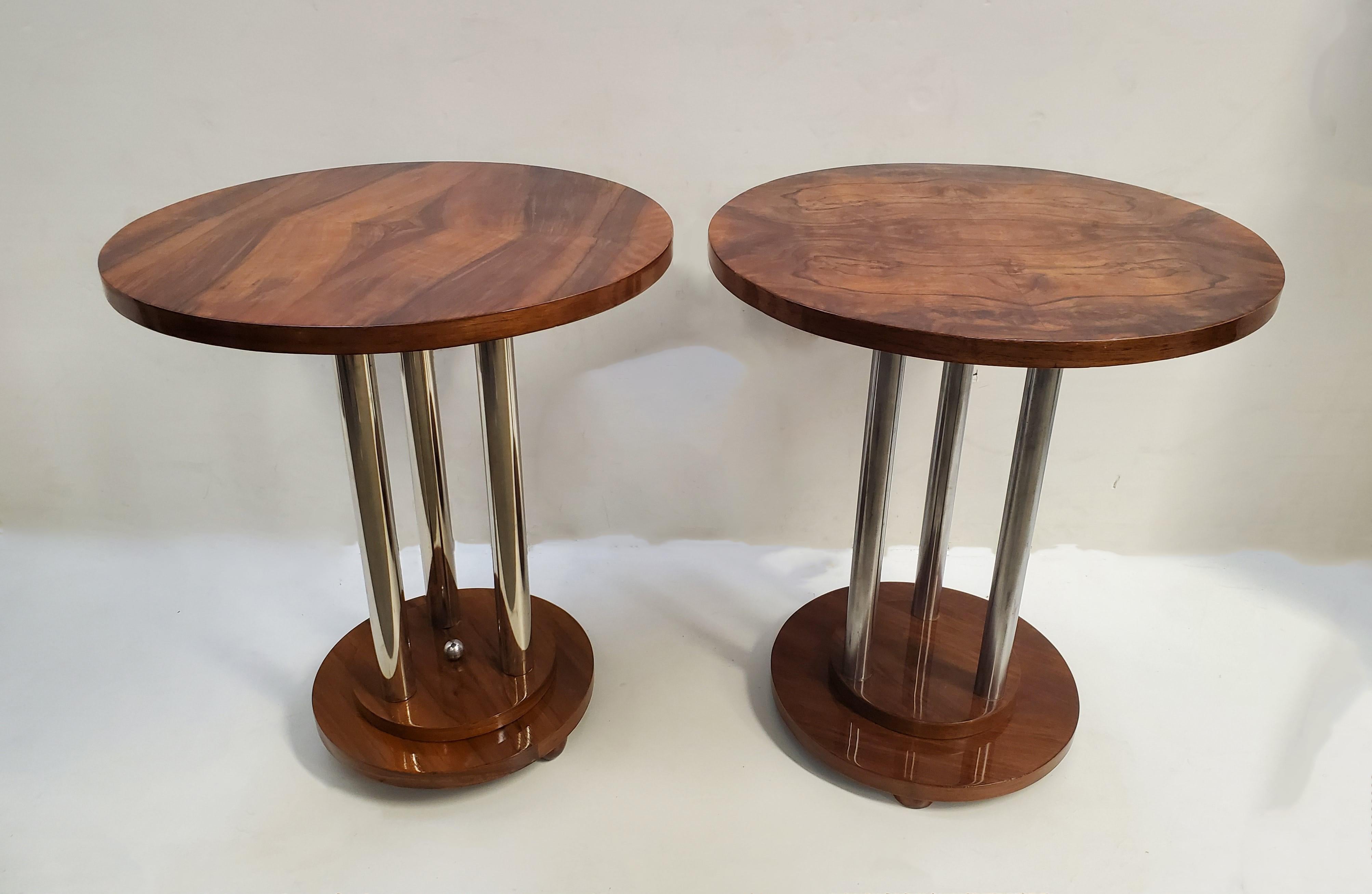 A similar pair of French Art Deco walnut side tables highlighted by nickeled metal accents. 
Three tubular metal poles support a beautifully grained, book matched circular wood top and rest on a circular stepped base ending with small toupie