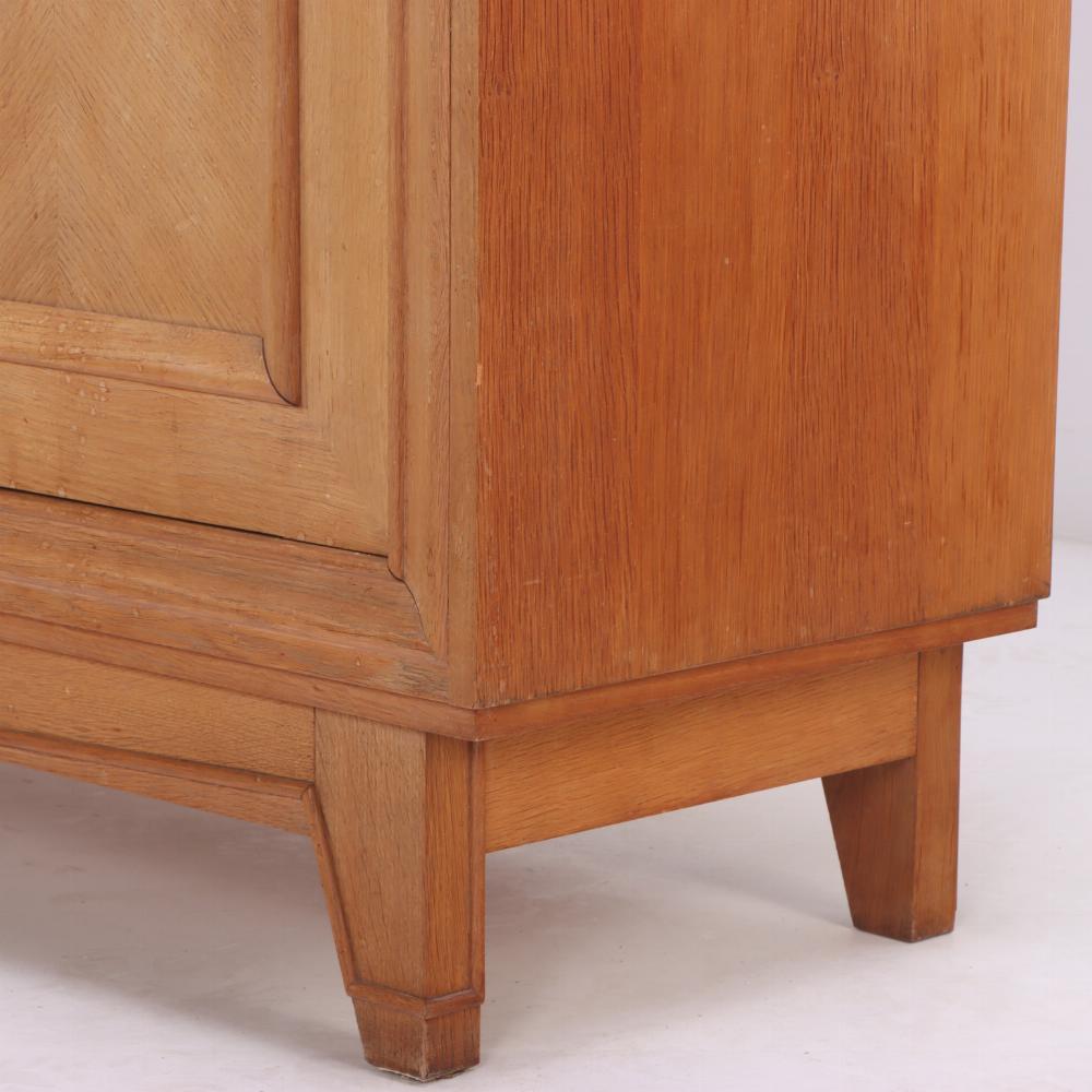 The light finish and the simple rectilinear design is perfect for today's interiors. The case has three doors that open to reveal a central drawer and shelves, all resting on recessed base with flared square tapering legs. Ample storage for use