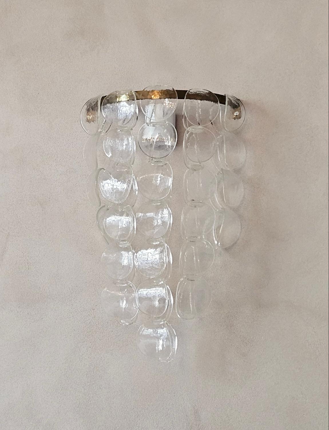 Une superbe applique murale en verre de Murano trouvée à Ravenne. L'applique est composée d'un cadre en laiton incurvé auquel sont suspendus 5 longueurs de liens en verre soufflé de Murano entrelacés à la main. Nous avons fourni quelques photos de