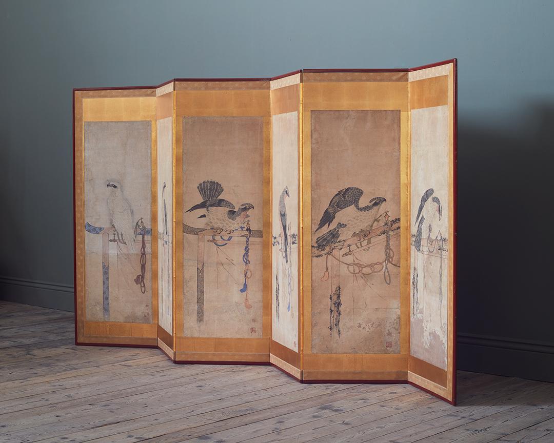 Six gouache painted scenes of tethered hawks, laid down to form a six panel screen, with pigment and ink on rice paper, surrounded by thickly set gold leaf border, and Japanese silk outer bordered wooden frame. Late Edo (1615-1868) – Meji period