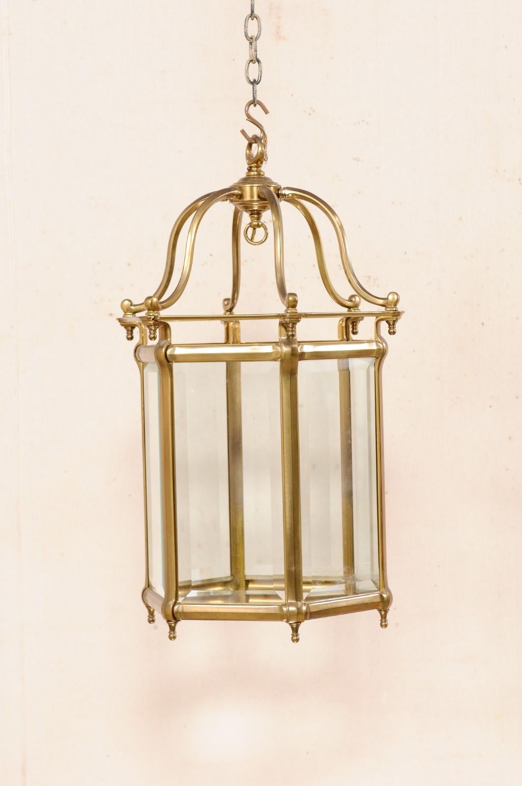 A single neoclassical style brass lantern. This vintage lantern is American-made with a nod to Neoclassism. It features a domed top, created from armature, a hexagonal body with beveled glass panels, and petite ball finial accents adorning the top