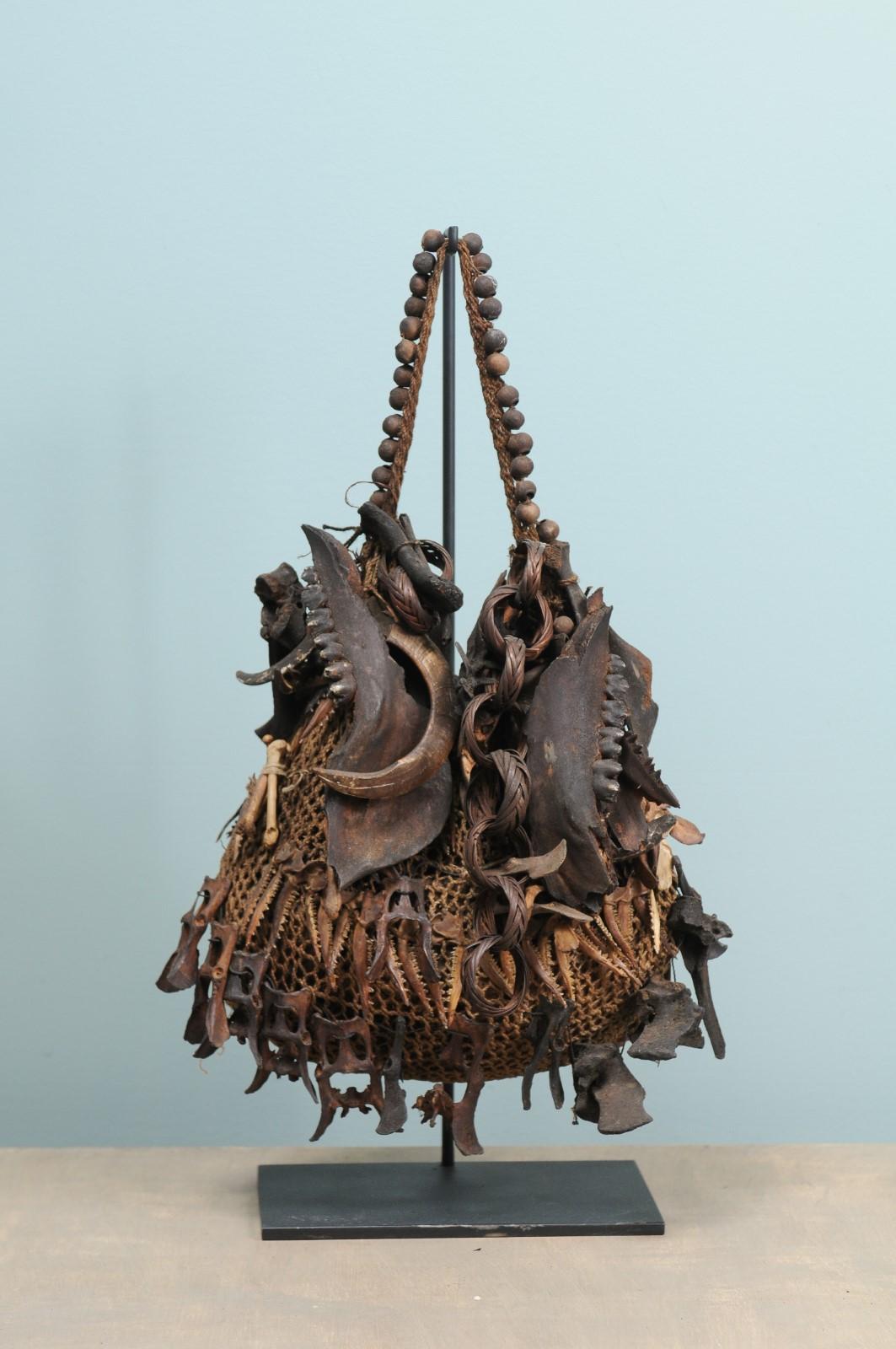 A single Papua New Guinea medicine bag from the mid-20th century on custom stand. This woven medicine bag from East Highlands Papua New Guinea features a nicely beaded handle strap, and is adorn with a collection of bones (some intricately carved),
