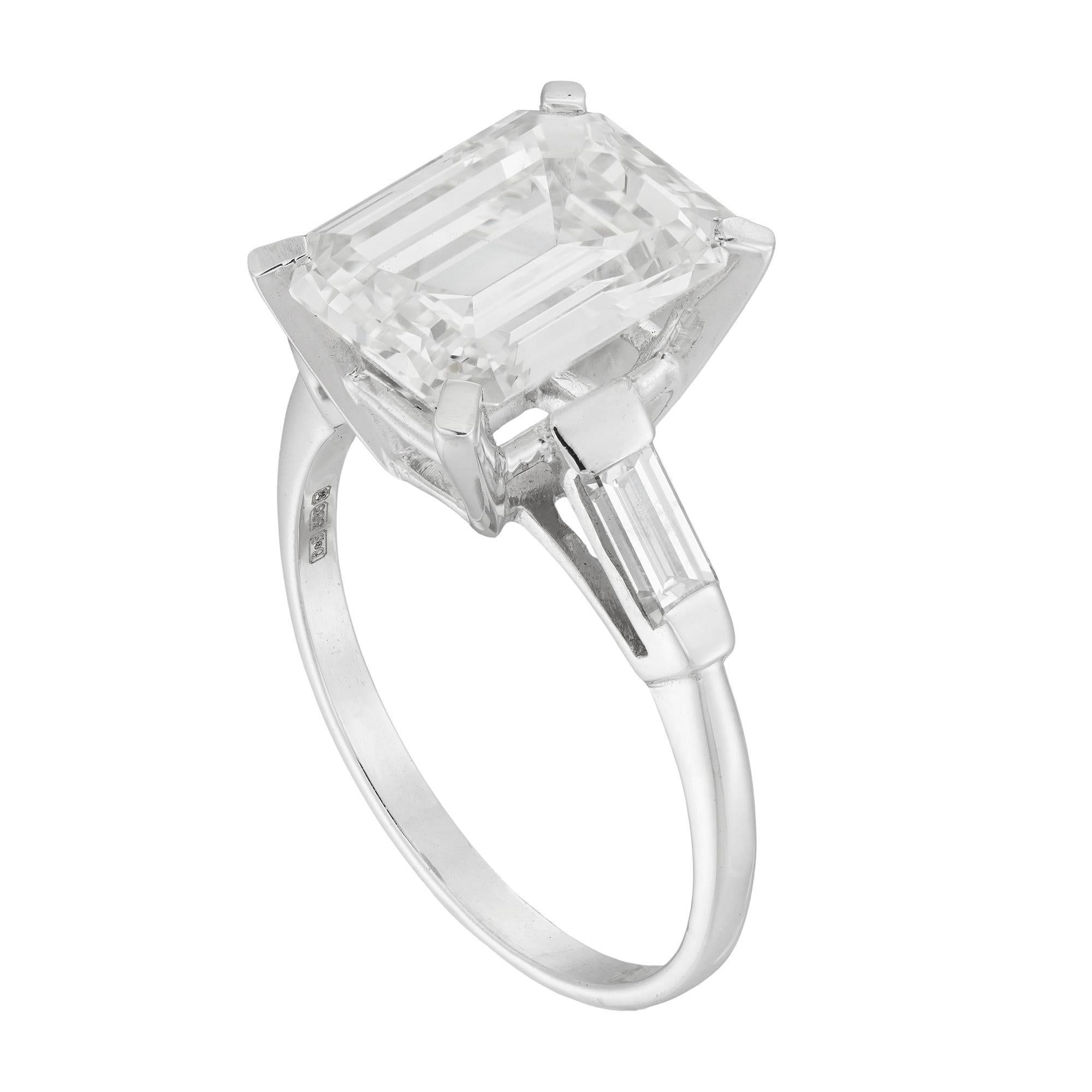 Anello con diamante taglio smeraldo a pietra singola, con diamante taglio smeraldo allungato del peso di 5,13 carati, accompagnato da un rapporto DeBeers che ne attesta il colore J e la purezza VS1, quattro griffe incastonate su una doppia pinza a