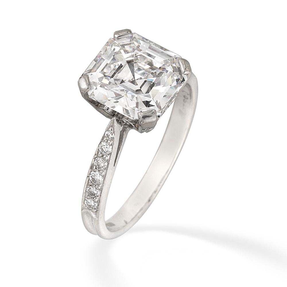 A single stone diamond ring, the square emerald-cut diamond weighing 3.07 carats, of E colour VS1 clarity, GIA certificate, four claw-set to a scroll pierced collet, with ribbed shank and round brilliant-cut diamond-set tapered shoulders, stamped