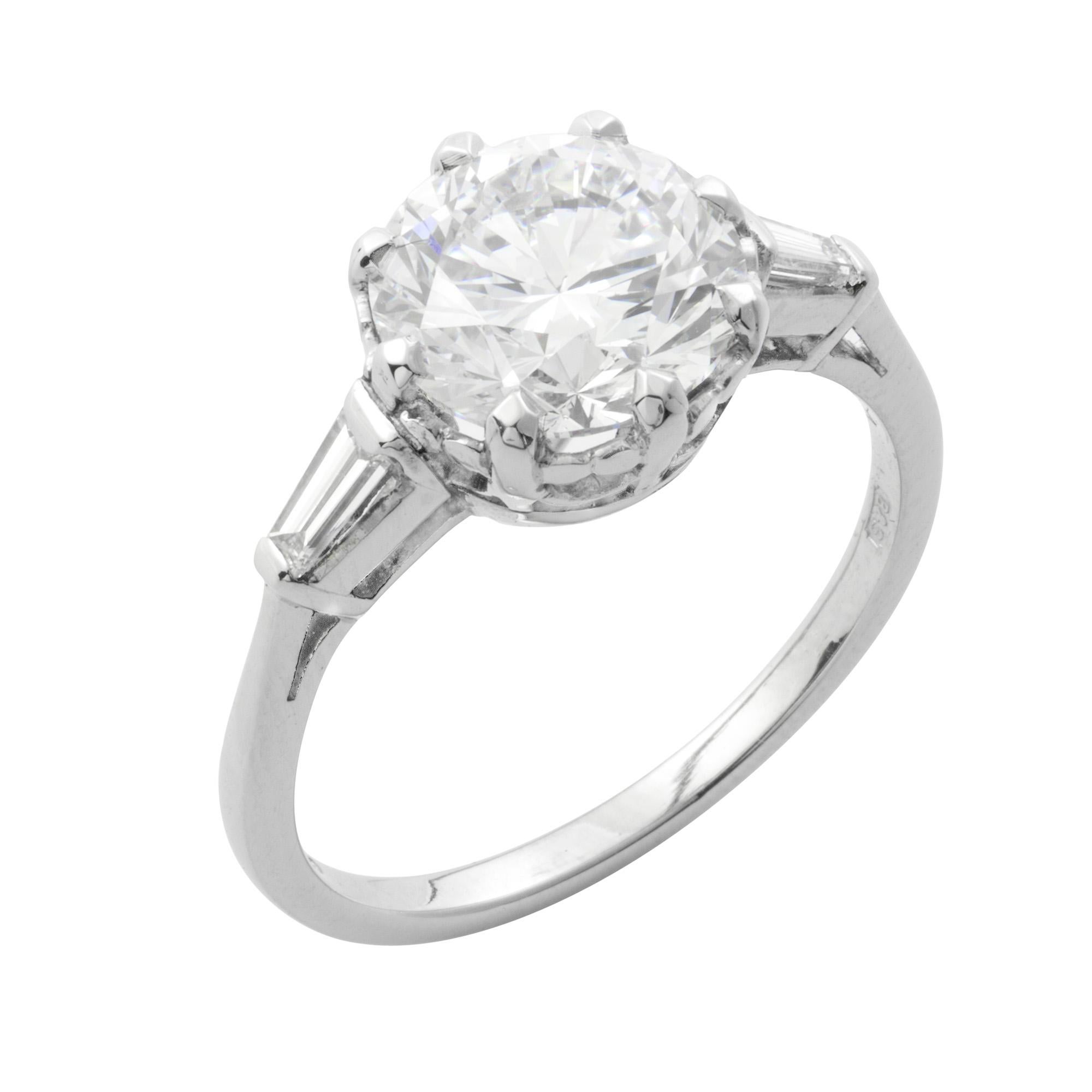 A single stone diamond ring, the round brilliant-cut diamond weighing 3.19 carats, of G colour and VVS2 clarity, accompanied by GIA Certificate, to an eight claw setting and a platinum scroll collet with a tapered baguette-cut diamond set to each