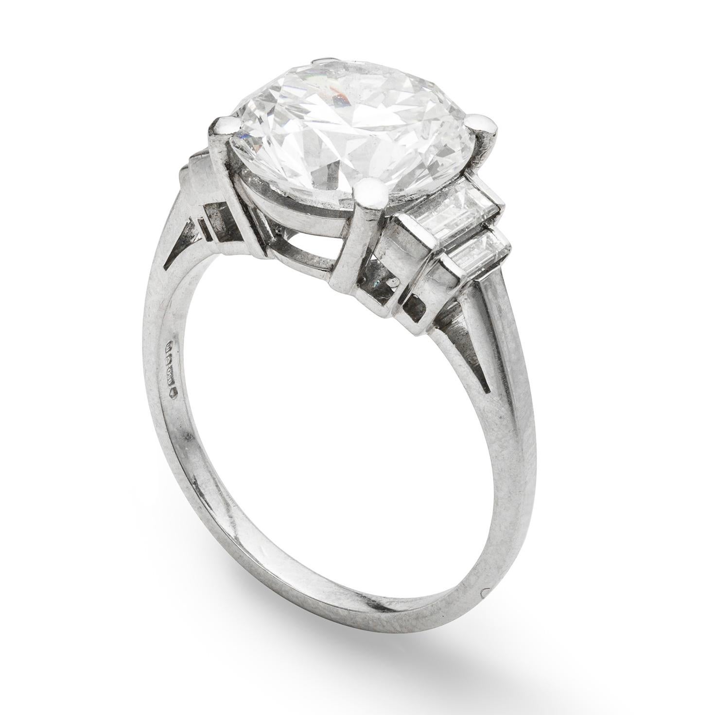 A single stone diamond ring, the round brilliant-cut diamond weighing 3.98 carats and of G colour and VS2 clarity, accompanied by GIA Certificate, four claw-set to an open double bar gallery between stepped baguette diamond shoulders all mounted in