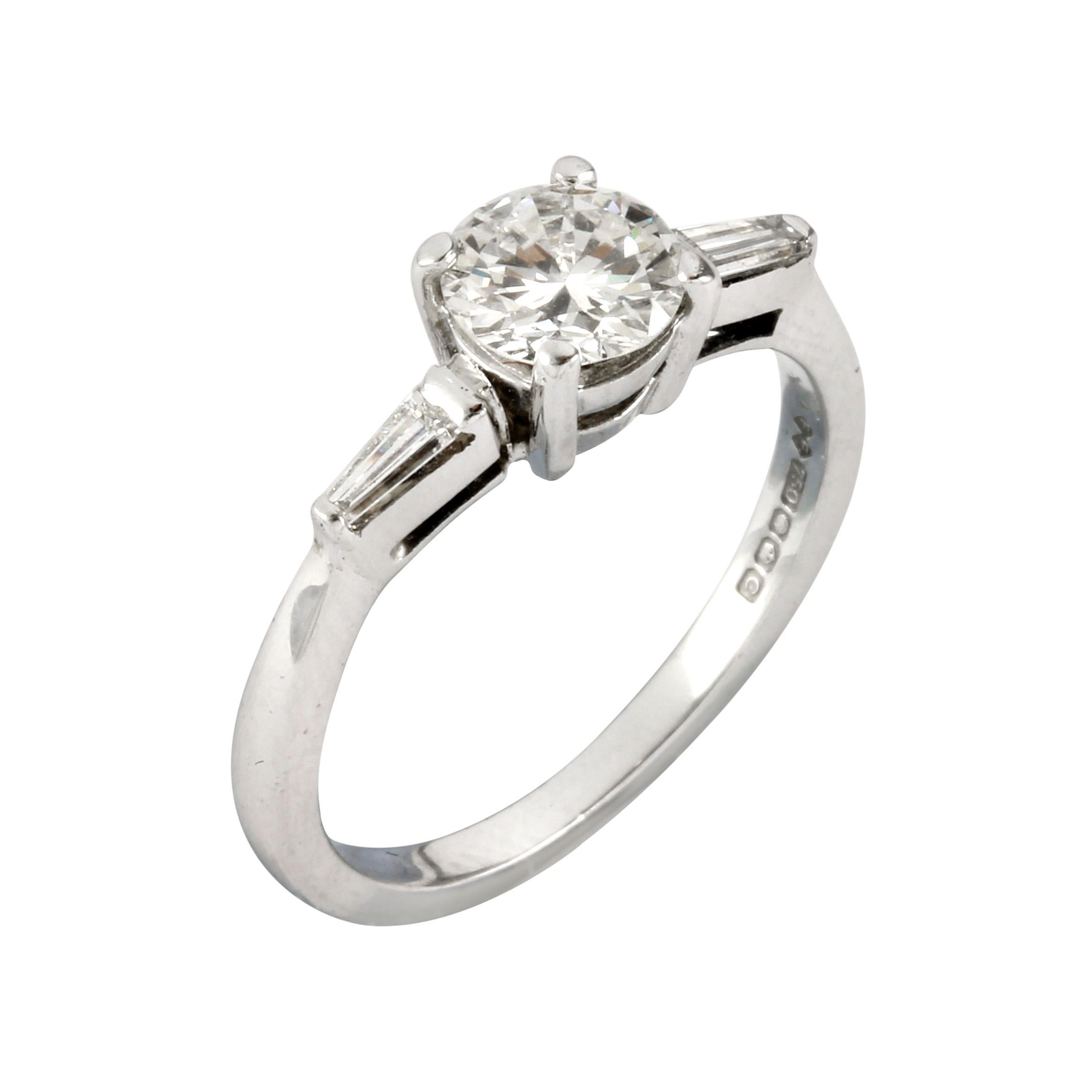 A single stone diamond ring, the round brilliant-cut diamond weighting 0.67carats, of H colour and SI1 clarity, accompanied by De Beers Grading Report, to a four claw setting with tapered baguette-cut diamond set to each shoulder, hallmarked 18ct