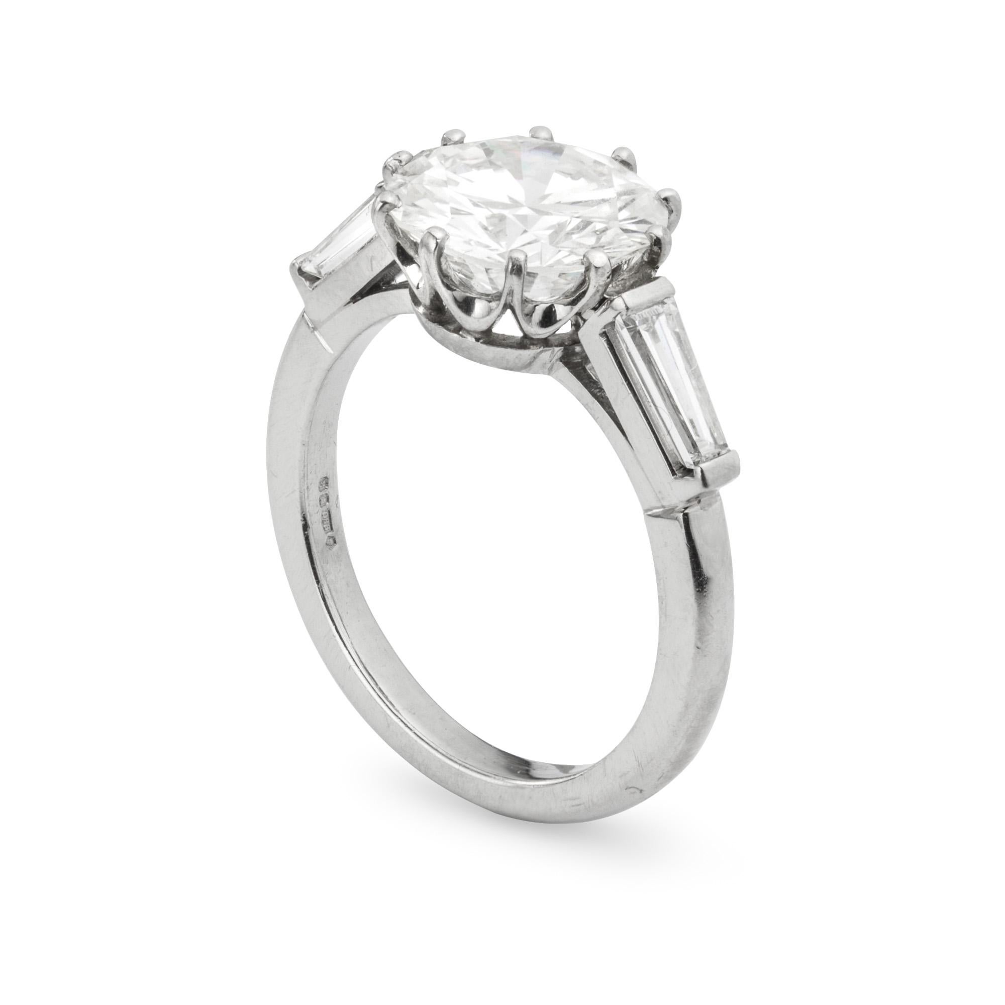A single stone diamond ring, the round brilliant-cut diamond weighing 3.04 carats, accompanied by GIA Certificate stating to be of H colour, SI1 clarity, ten claw-set to a  platinum crown collet, a tapered baguette-cut diamond set to each shoulder,