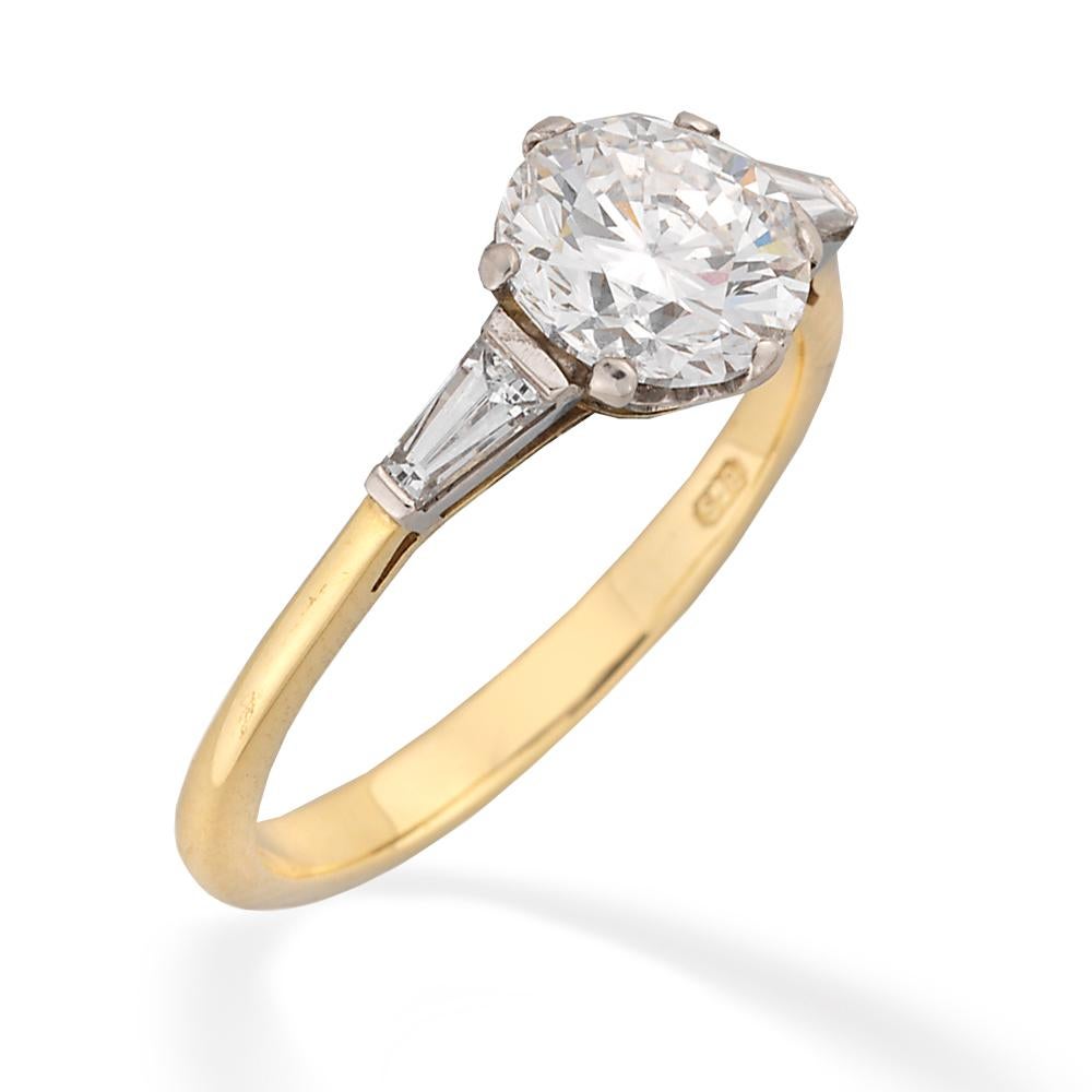 A single stone diamond ring, the round brilliant-cut diamond weighing 1.50 carats of F colour, VS2 clarity, GIA certificate, six claw-set to a white gold mount with scroll heart decoration to the gallery, a tapered baguette-cut diamond to each