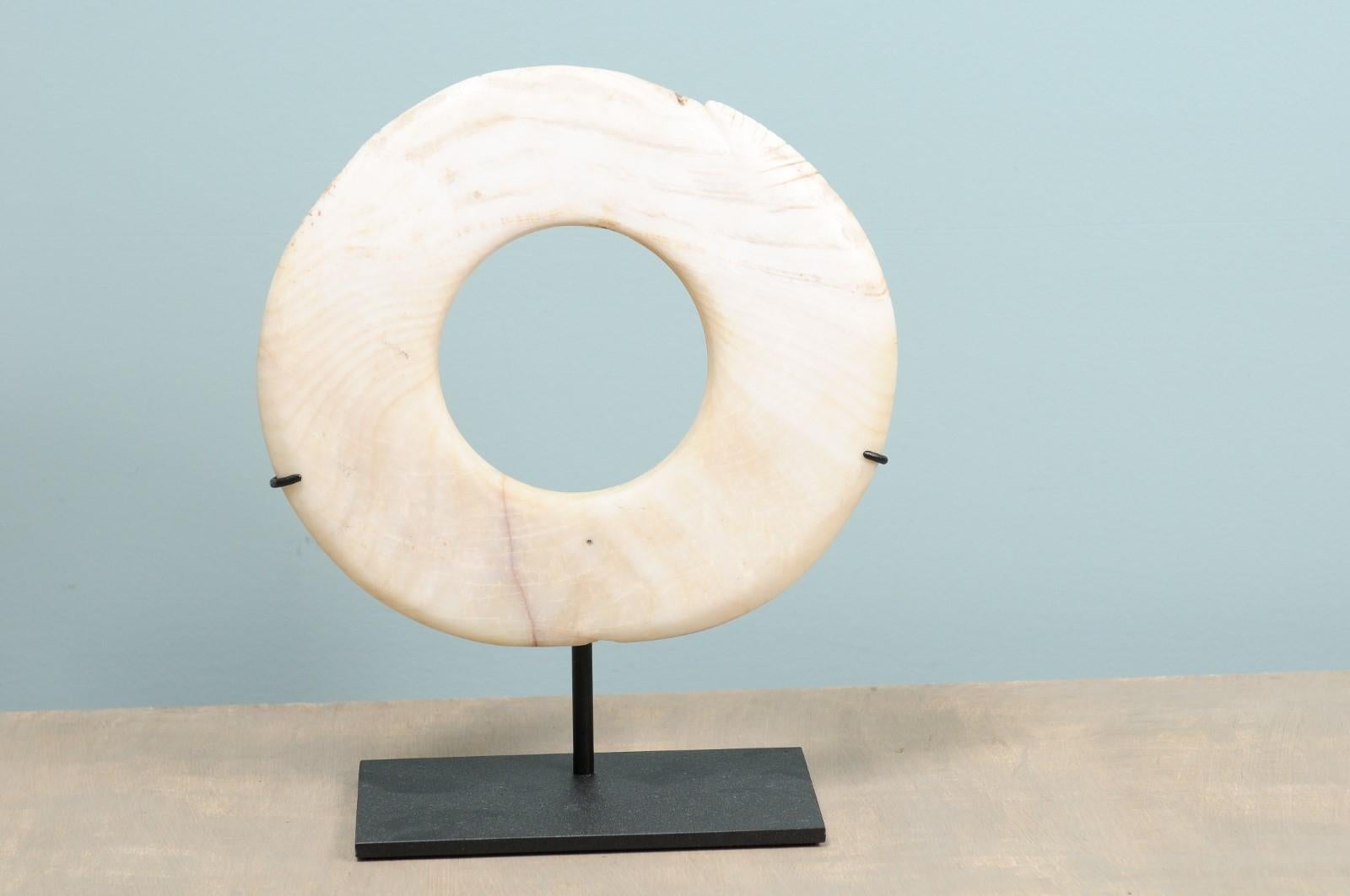 A single Yua Wenga currency from the early 20th century on custom iron stand. This antique tribal currency piece from Papua New Guinea has been carved from a giant clam shell, with pieces of bamboo. Yua means money and Wenga are clam rings. The Yua