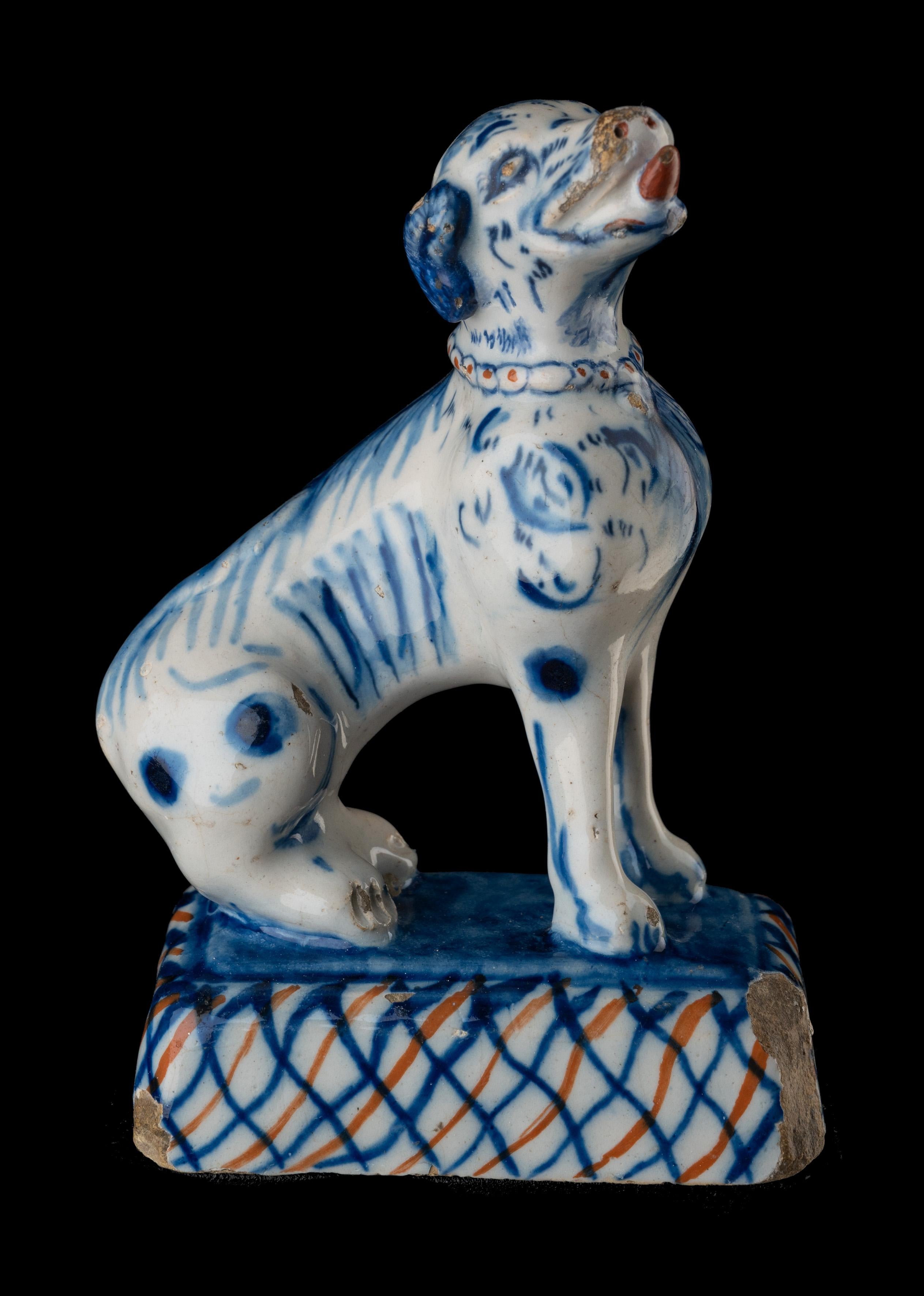 The molded dog is sitting on a rectangular base and has its head raised and turned, and his snout opened. He wears a red-dotted collar. The dog is painted in blue, the stand in blue and red. 
A nearly identical pair of dogs is in the Lavino