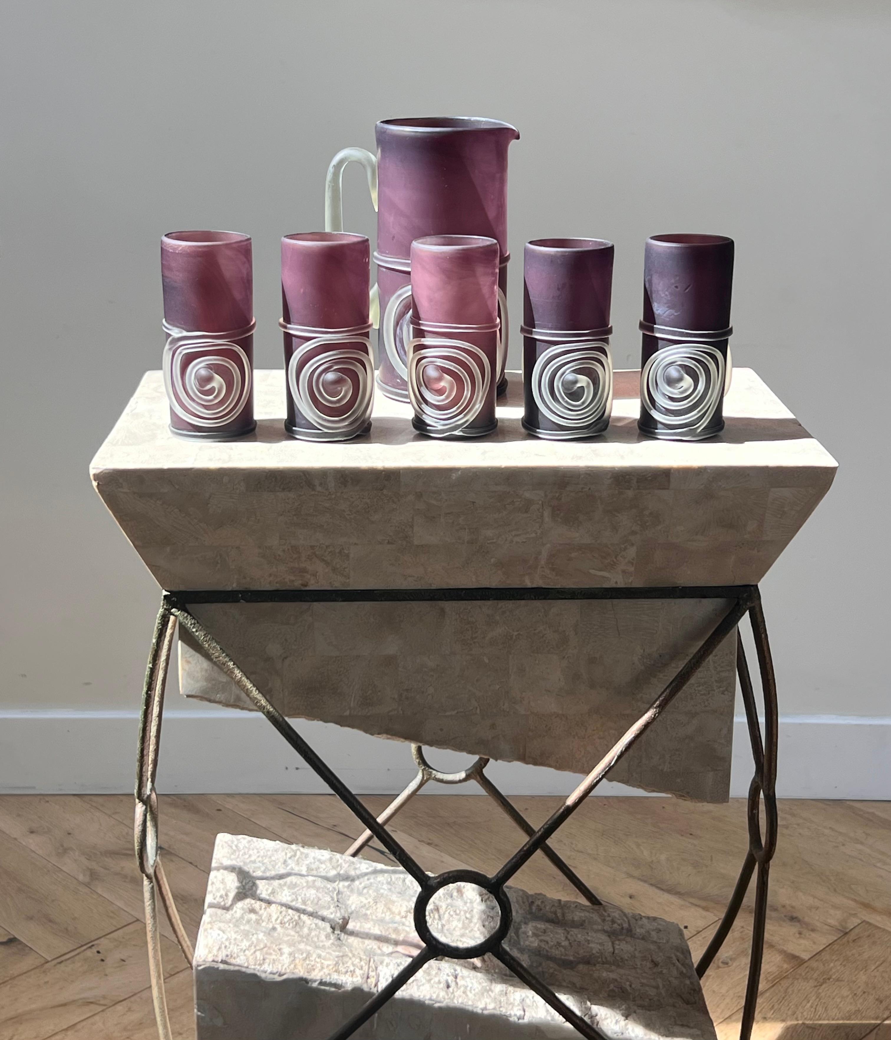 Ensemble composé de six pièces en verre d'art violet : un pichet et cinq gobelets, fin du 20e siècle. Probablement d'Italie. Chaque pièce présente une spirale complexe soufflée à la main en verre d'art dépoli. La nuance de violet est une belle