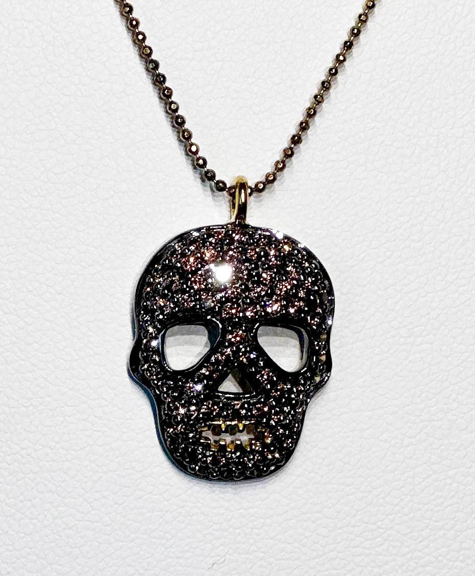 A Blackened Silver Skull Pendant set with  Brown Zircon, hanging from a gold plated 18