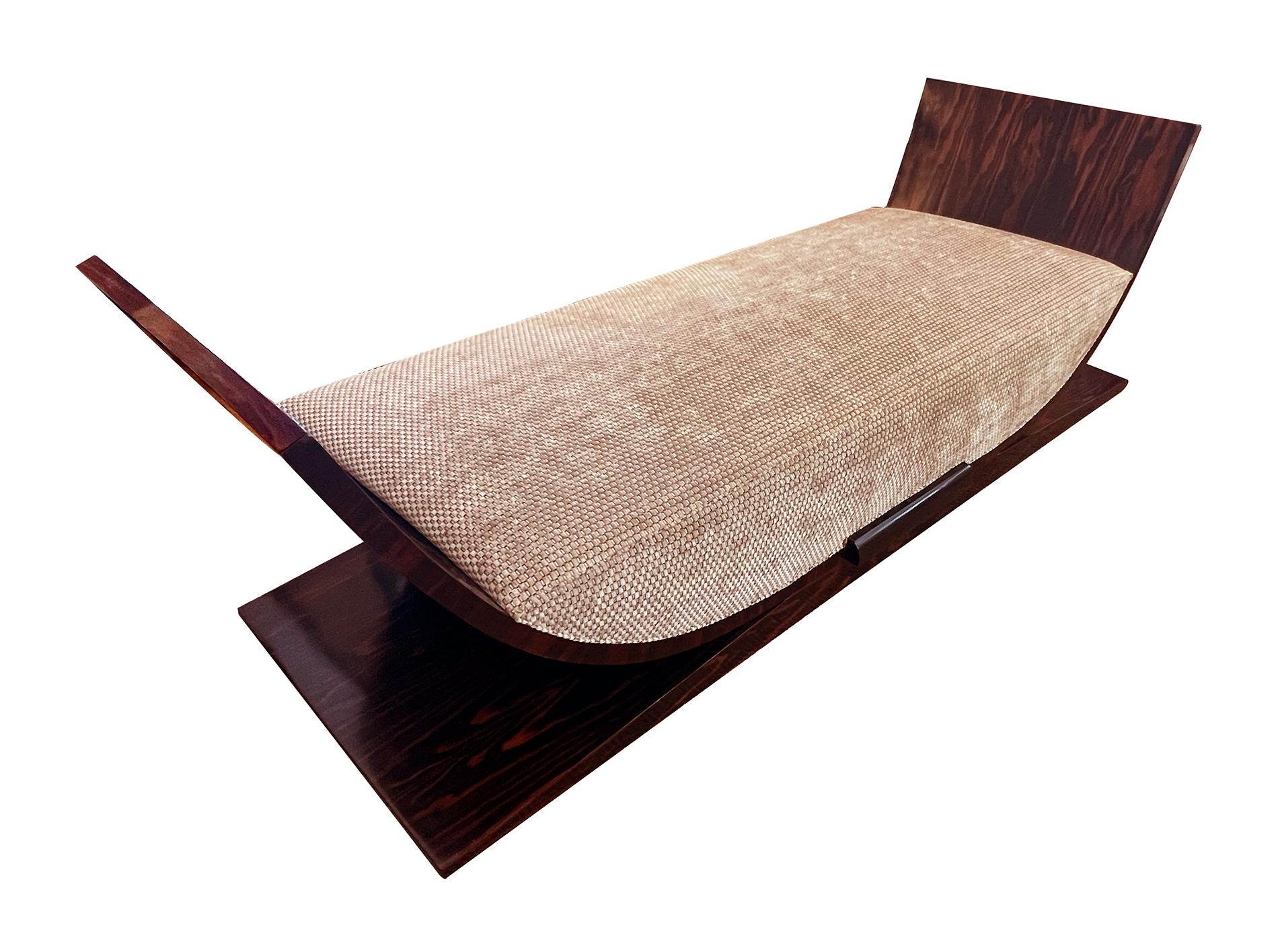 of well-figured macassar veneer with its dark chocolate brown and alternating irregular caramel color striations; the shapely daybed with dramatic incurved ends flanking a deep upholstered seat; raised on a sloping rectangular plinth