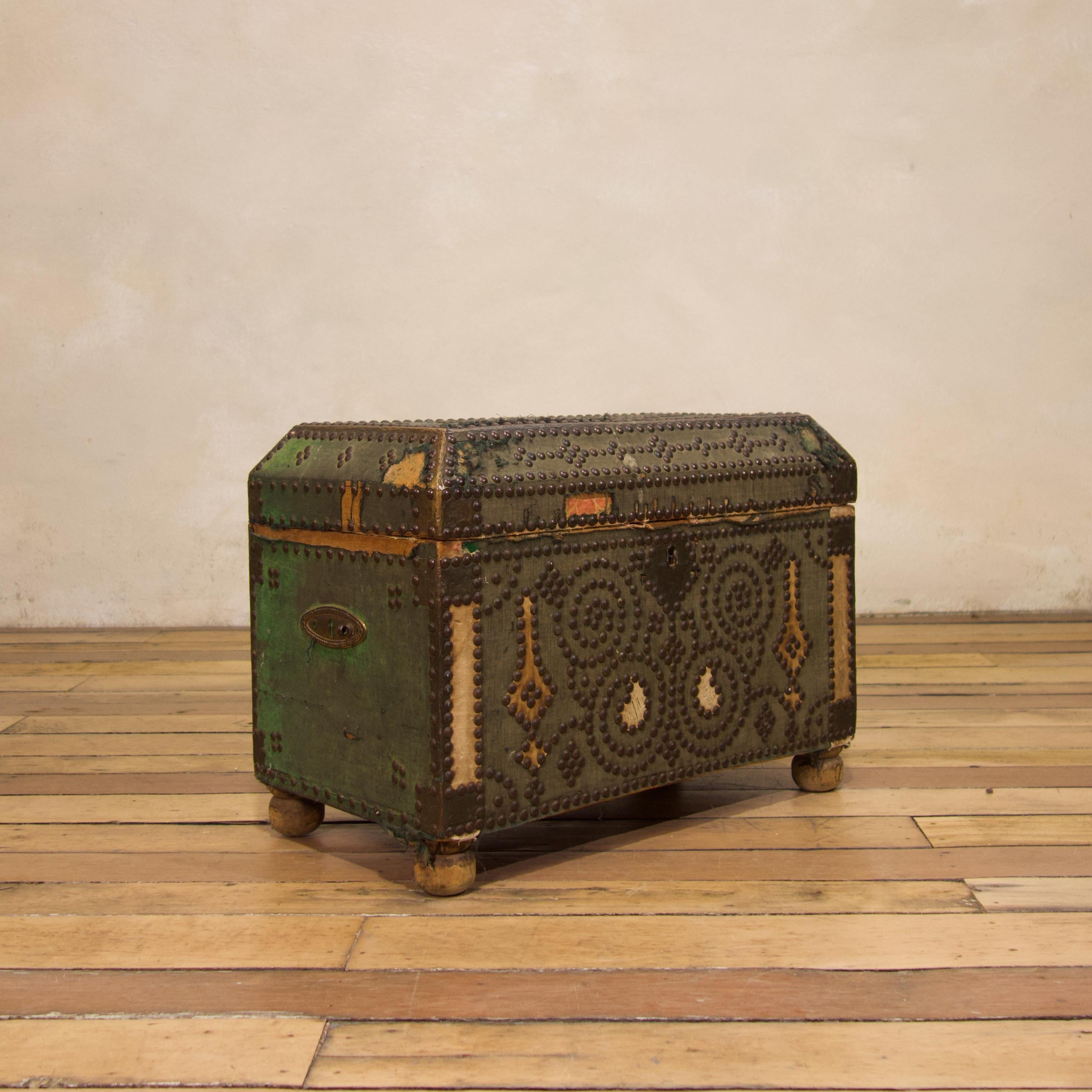 A small 19th century French studded and cloth-bound chest. Covered in the original green and white cloth decorated with brass studs and brass bound edges. Displaying a domed top, raised on bun feet. A charming small trunk that would lend itself