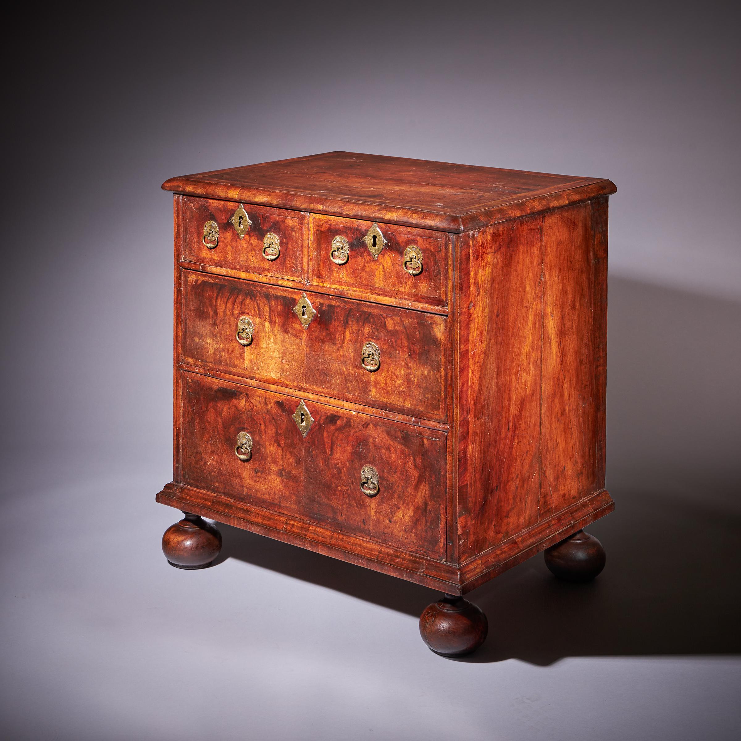A 17th-century William and Mary figured walnut chest of drawers of diminutive proportions, circa 1690-1700. England.

The cross-grain moulded, feather and crossbanded quarter veneered walnut top sits above two short and two long oak-lined graduating