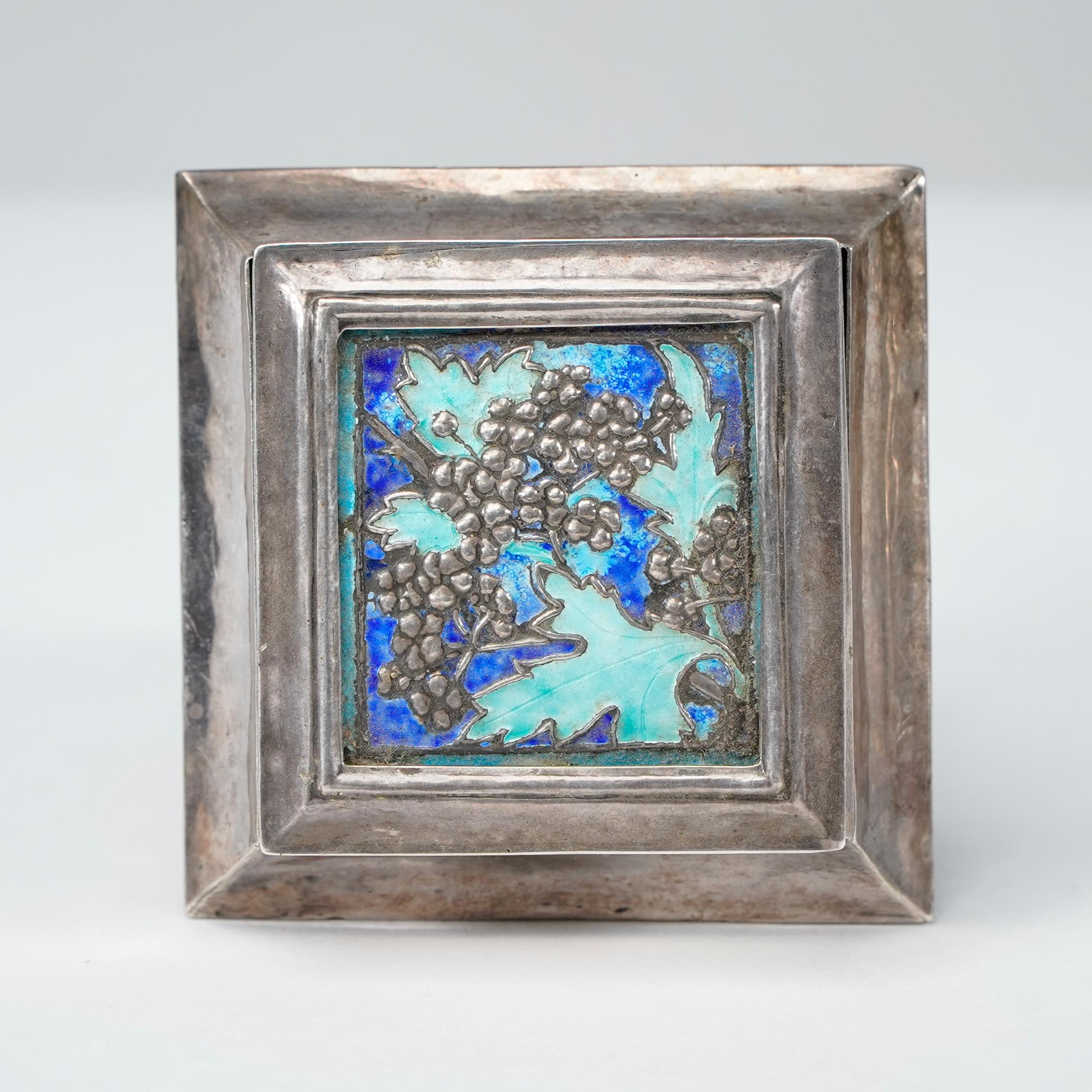 A small Arts and Crafts silver plated jewellery box with enamel decoration displaying grapes and leaves to the lid and shaped sides.
