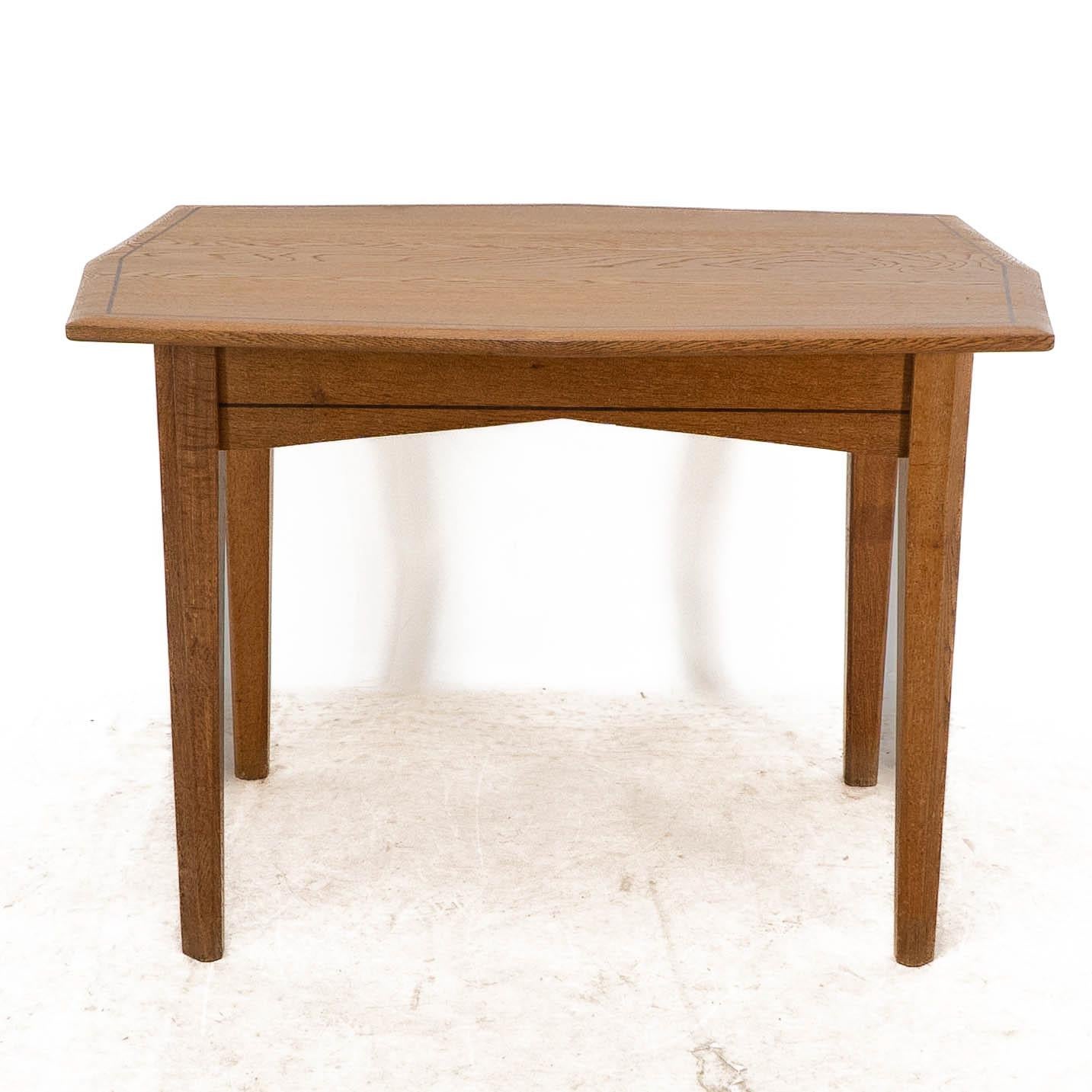 A small Arts and Crafts Cotswold style oak dining or centre table with subtle angular designs to the top and to the lower apron with ebonized line inlay to the top and to the apron. The legs with angular chamfered details.