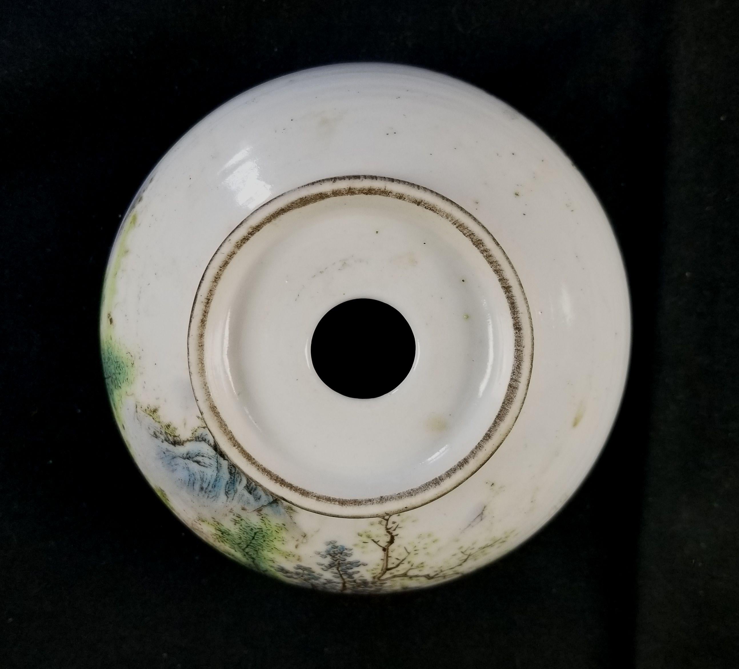 Un lavacepillos redondo de porcelana realmente fino, pintado a mano, con una escena de pueblo en la que la casa está enclavada en una zona de hierba rodeada de árboles, rocas, montañas y un río.

  