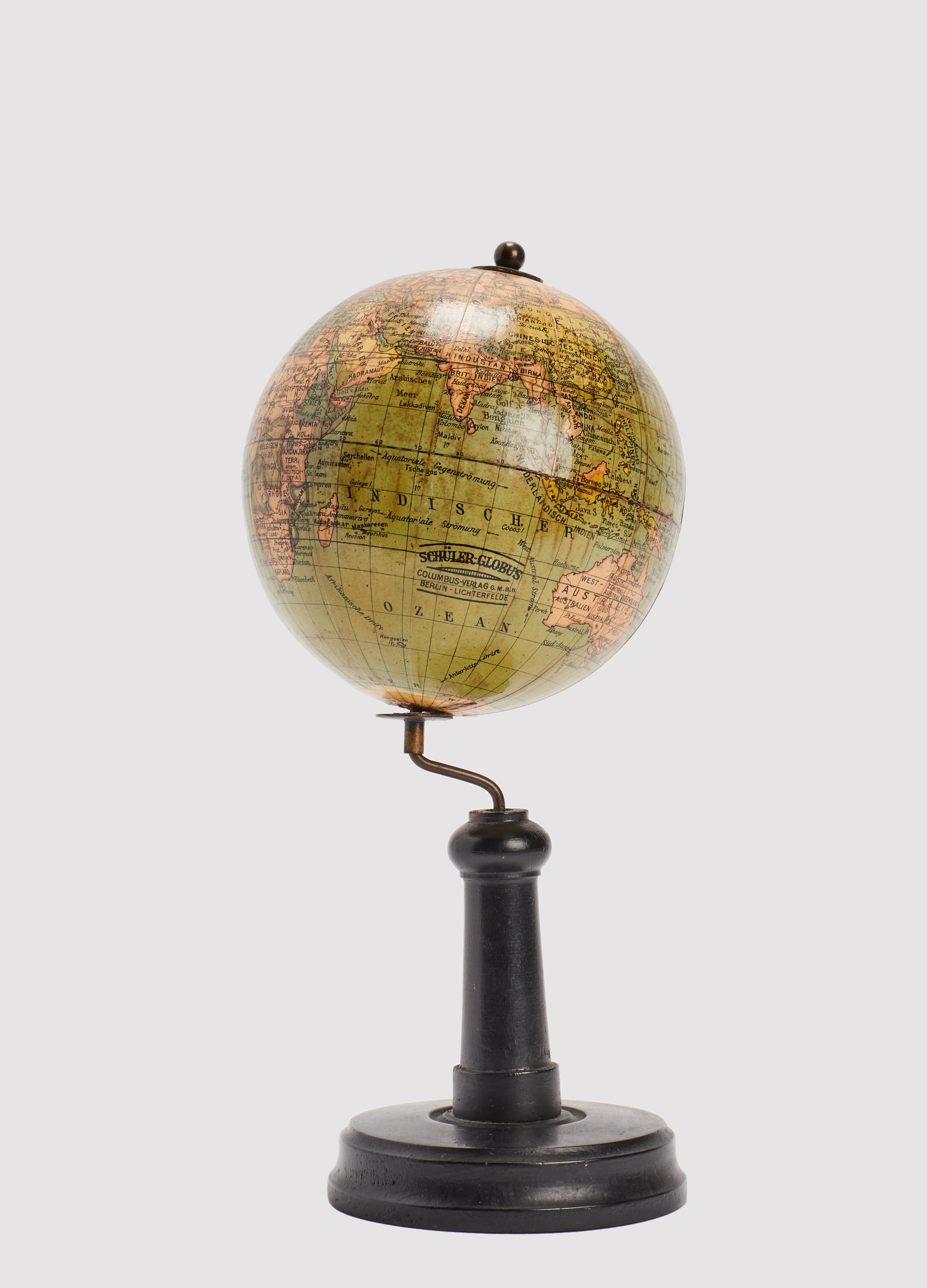 Auf einem gedrechselten Holzsockel mit rundem Fuß, gewelltem Profil und hohem Bein, mit originaler Patina, befindet sich ein kleiner Globus, herausgegeben von Columbus, Berlin. Die Weltkugel ist aus Pappmaché gefertigt, mit einem feinen Kleister
