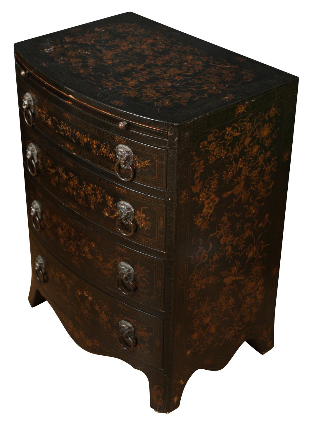 A great little size, this piece can be used as a side table, night table or in a small entry. Featuring four drawers with lion head pulls, the item has an ebonized finish decorated in a gold floral motif. The scalloped apron and pull-out tray add