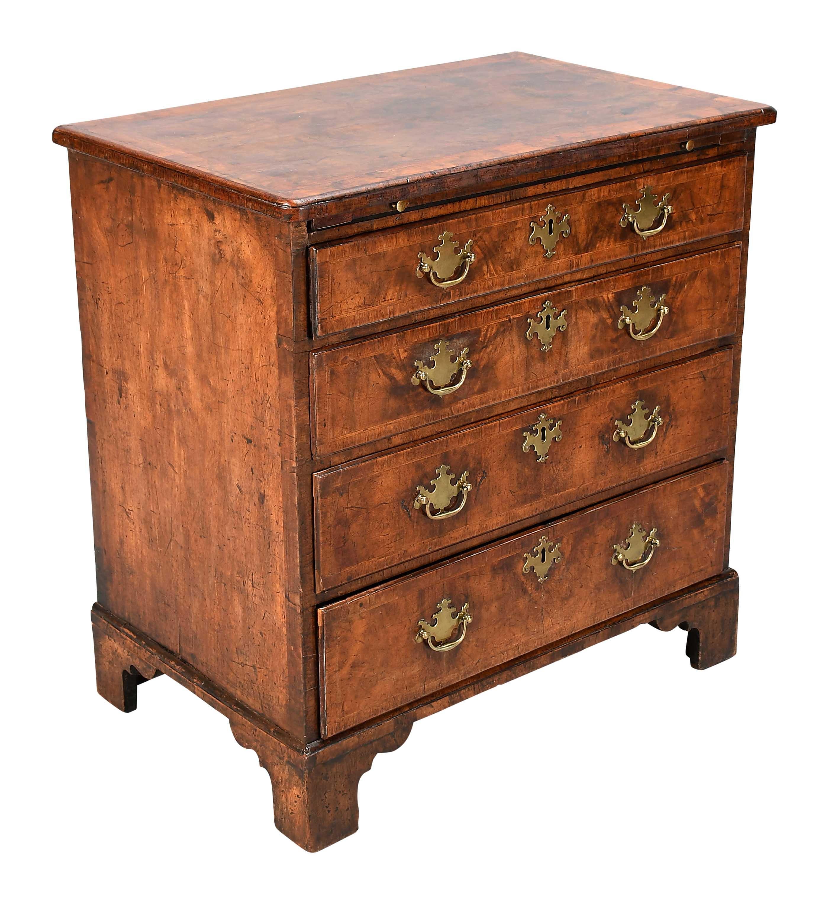 A small chest with a brushing slide over four graduated drawers fitted with the original hardware. The well-figured walnut veneers retain a lovely color and patina. The quarter-veneered top and the drawer fronts are feather-banded and cross-banded.