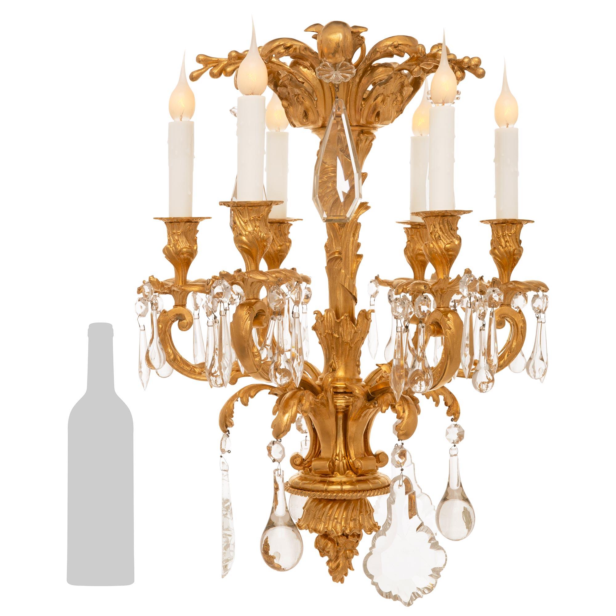 








A small French 19th century Louis XV st. Ormolu and Crystal chandelier. The six arm chandelier displays a central fut decorated with foliage amidst a twisted ribbon. The fut is surrounded by the six scrolled arms leading to the scalloped